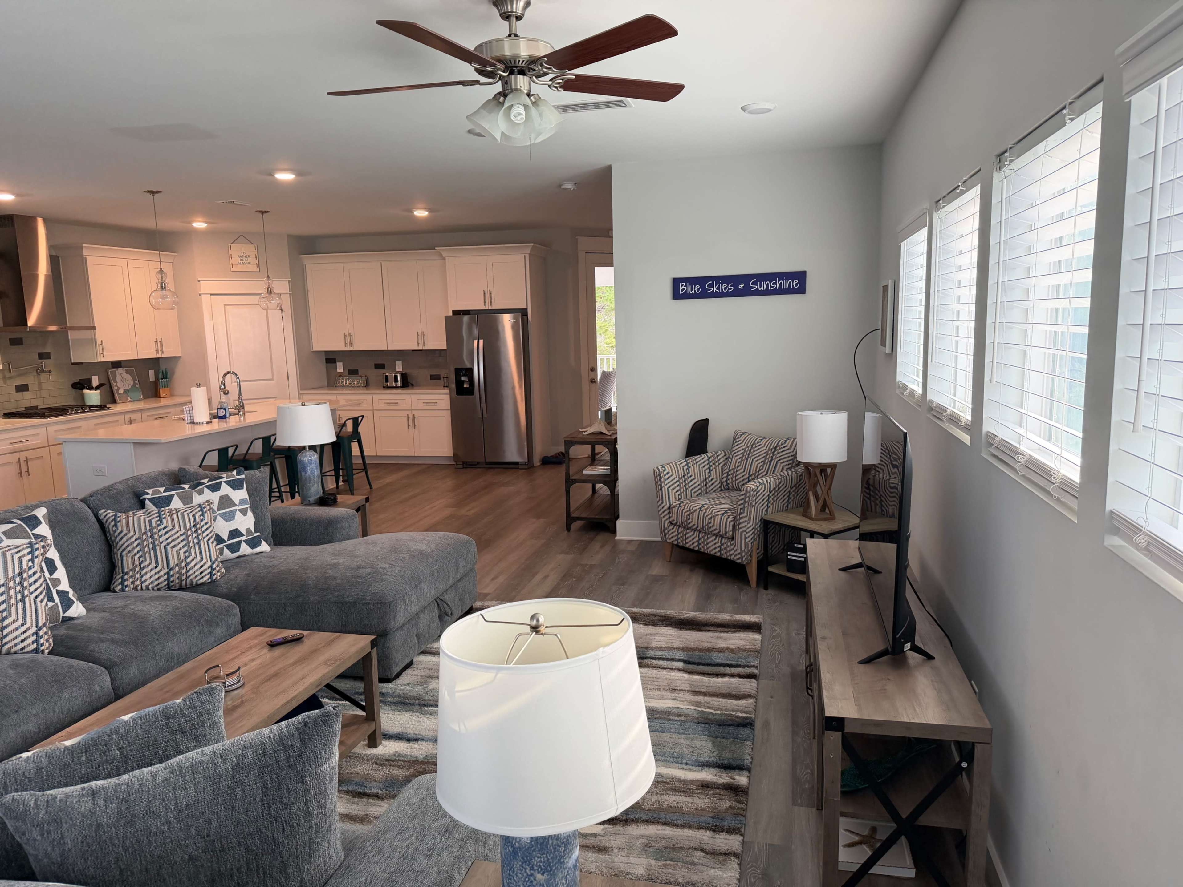 The living room features a sectional sofa, two armchairs, a coffee table, and a television, all arranged around a light-colored wooden floor.