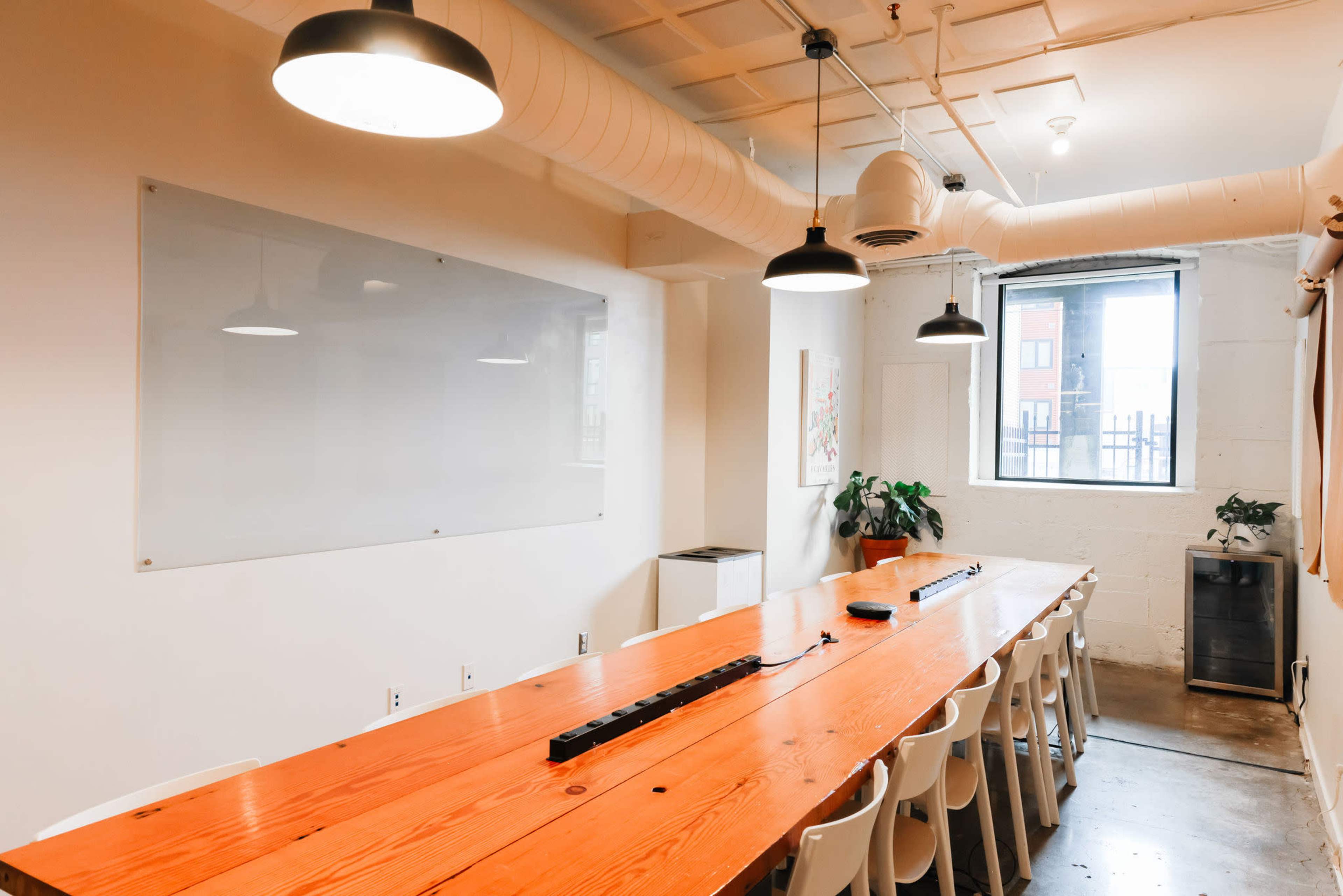 A large conference room features a long wooden table surrounded by white chairs, with a whiteboard and a window on one side.