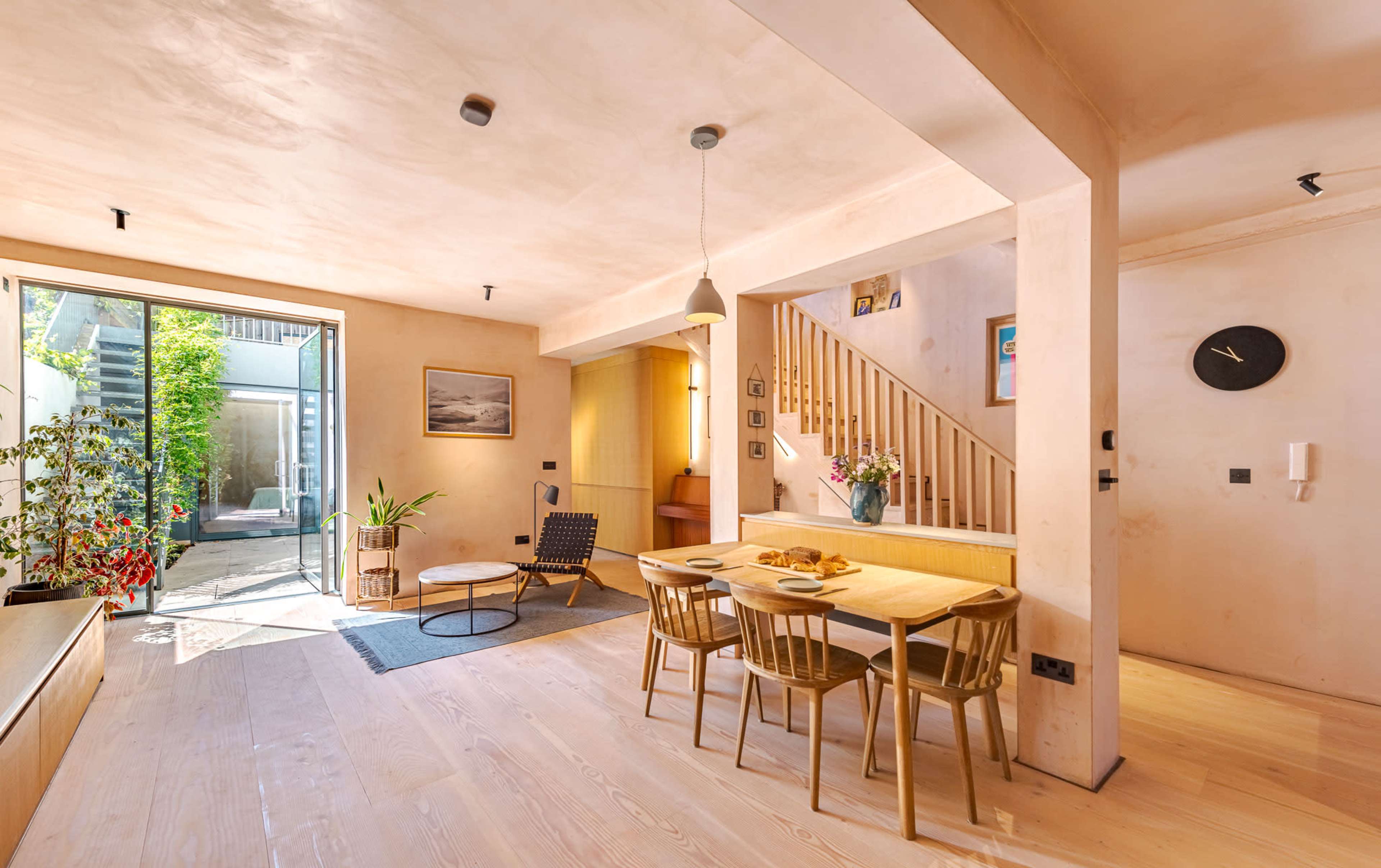 A modern open-plan living space with a dining area, a staircase, and large windows leading to an outdoor garden.