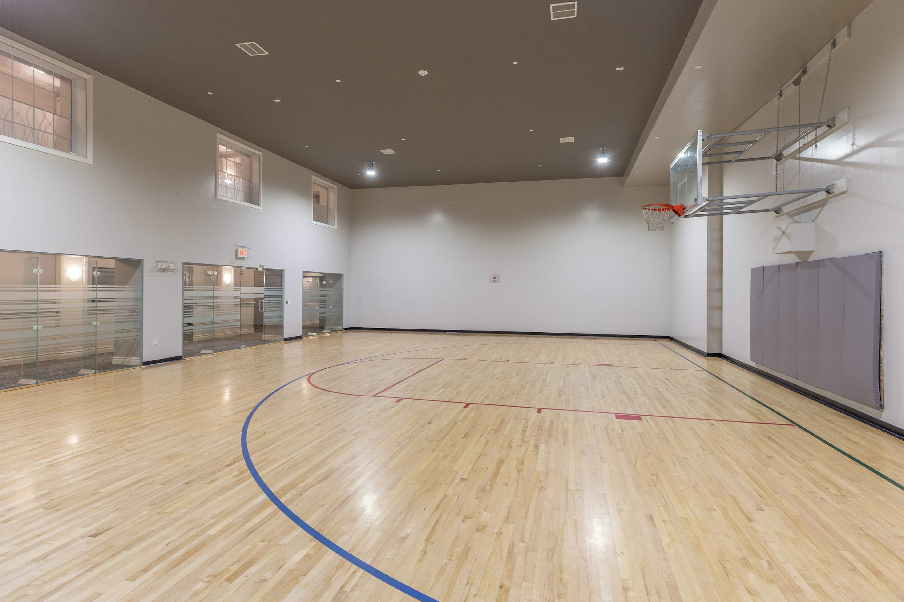 An empty indoor basketball court with a single hoop mounted on the wall.