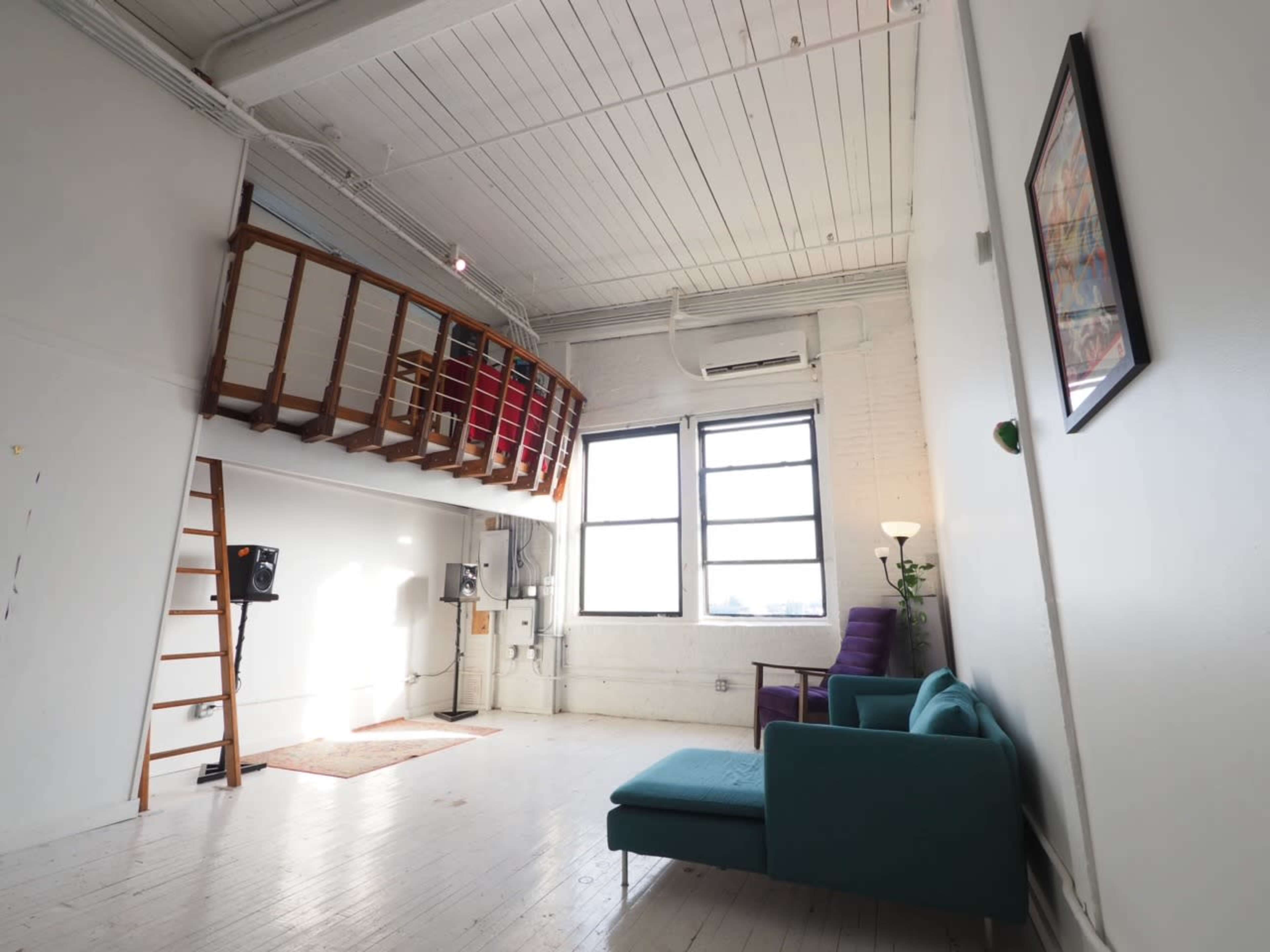 The image shows a spacious, well-lit room with a loft area, a green sofa, a purple chair, and a wooden ladder leading to the loft.