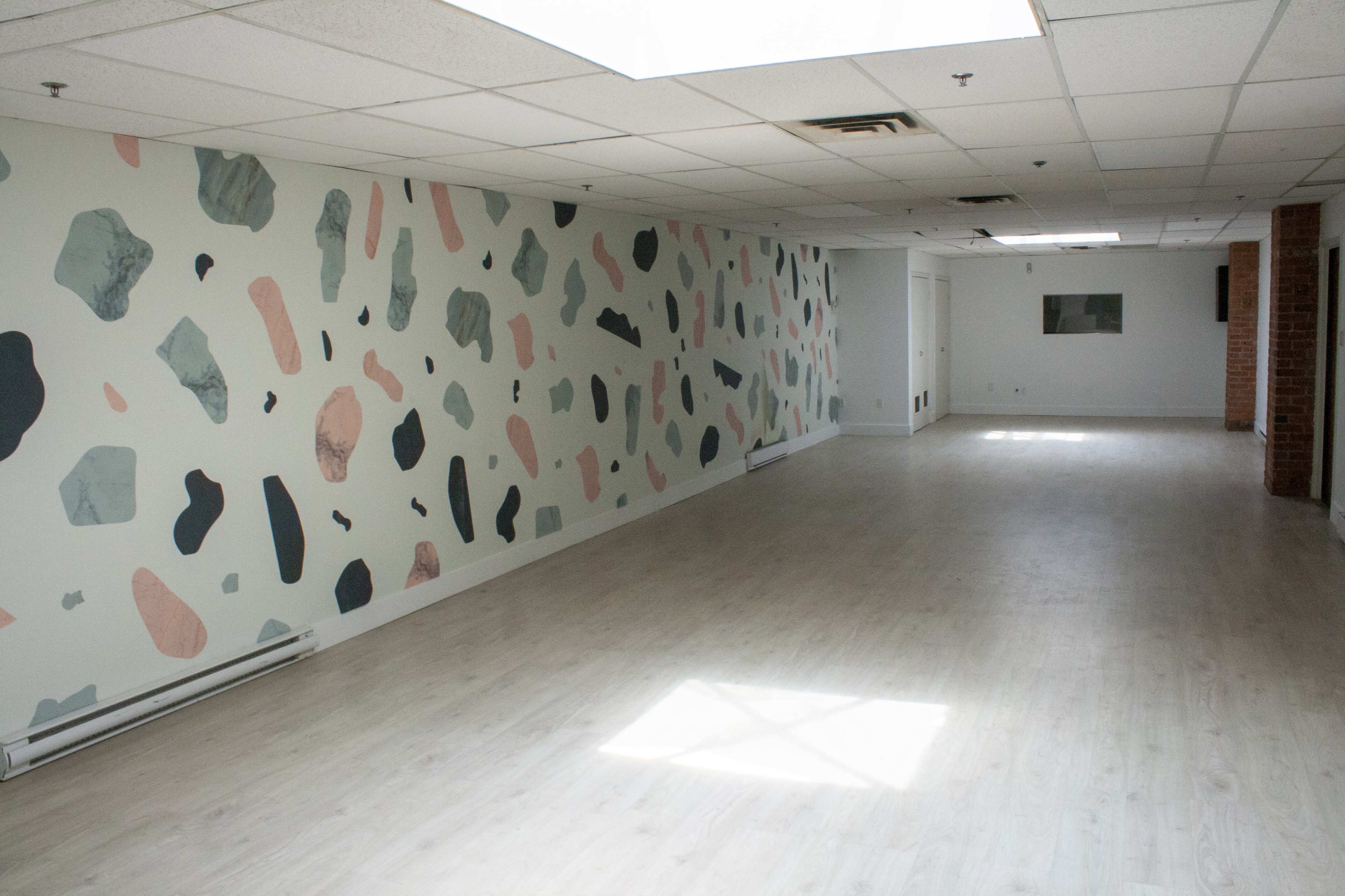 An empty room with a light-colored floor and a wall decorated with abstract shapes in various colors.