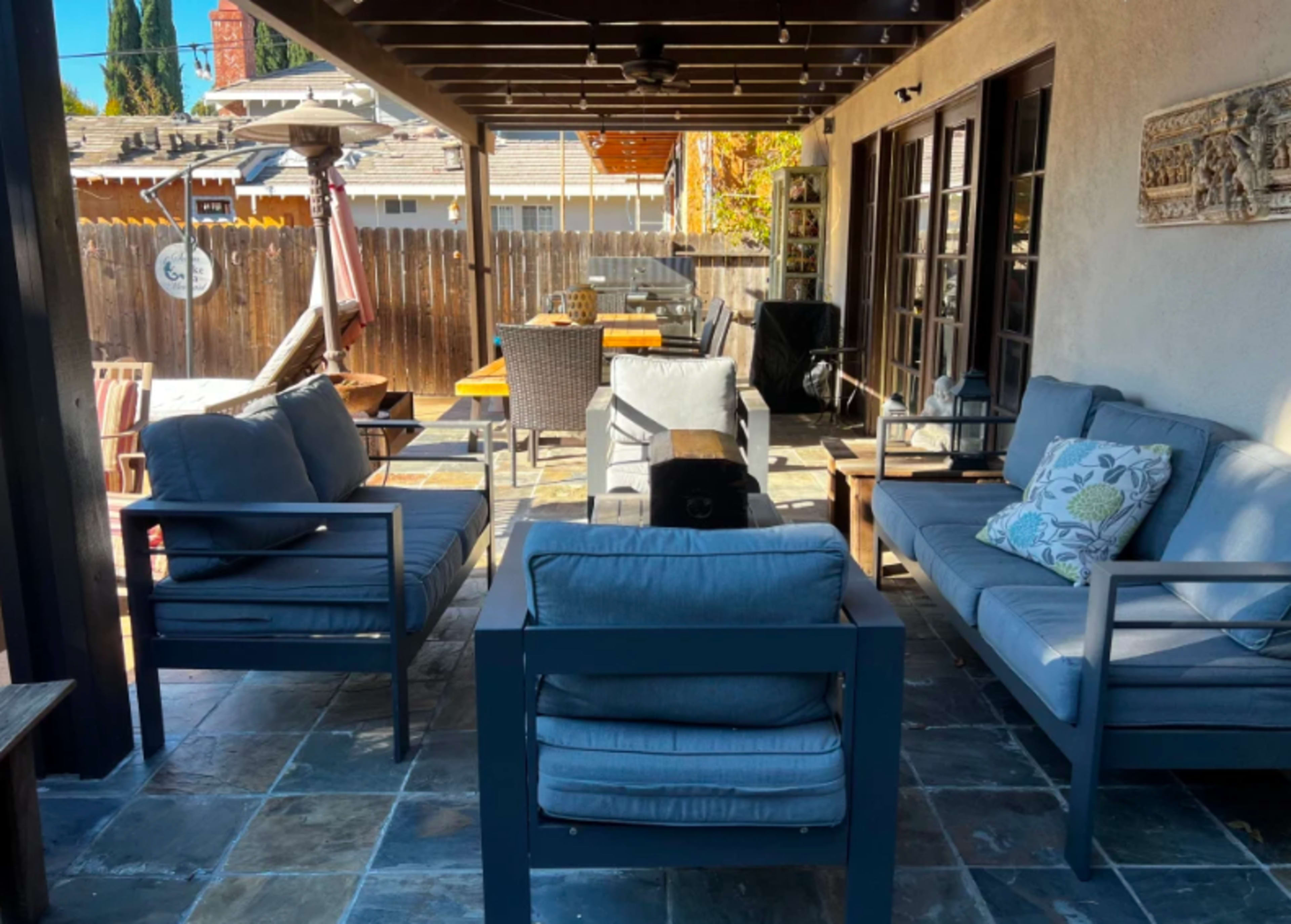 A patio area features gray outdoor seating arranged around a stone floor and a wooden table.