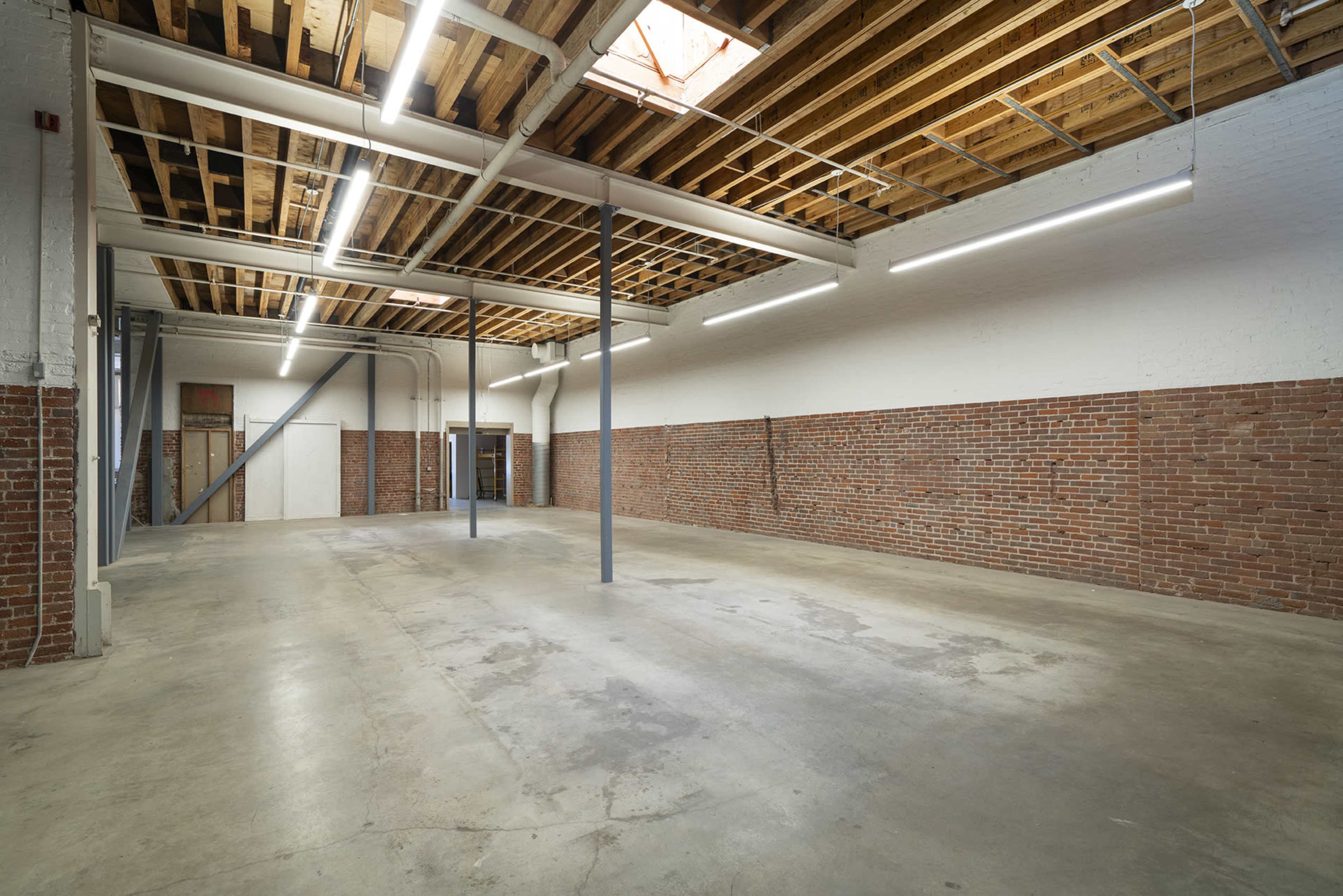 A vacant industrial space with exposed brick walls, a concrete floor, and wooden beams overhead.