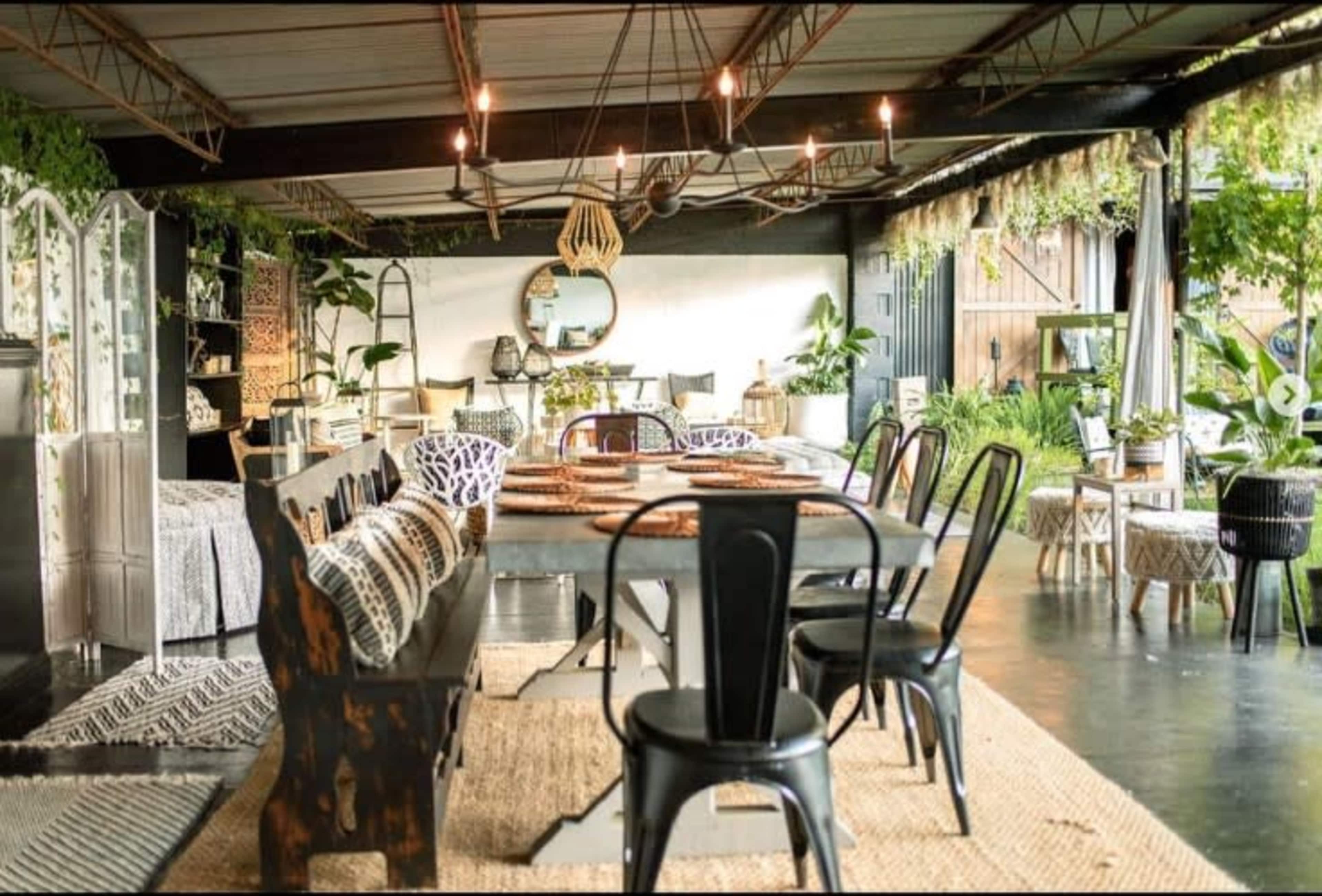 A modern indoor dining area featuring a large dining table surrounded by black metal chairs, with decorative plants and stylish decor pieces in a spacious setting.