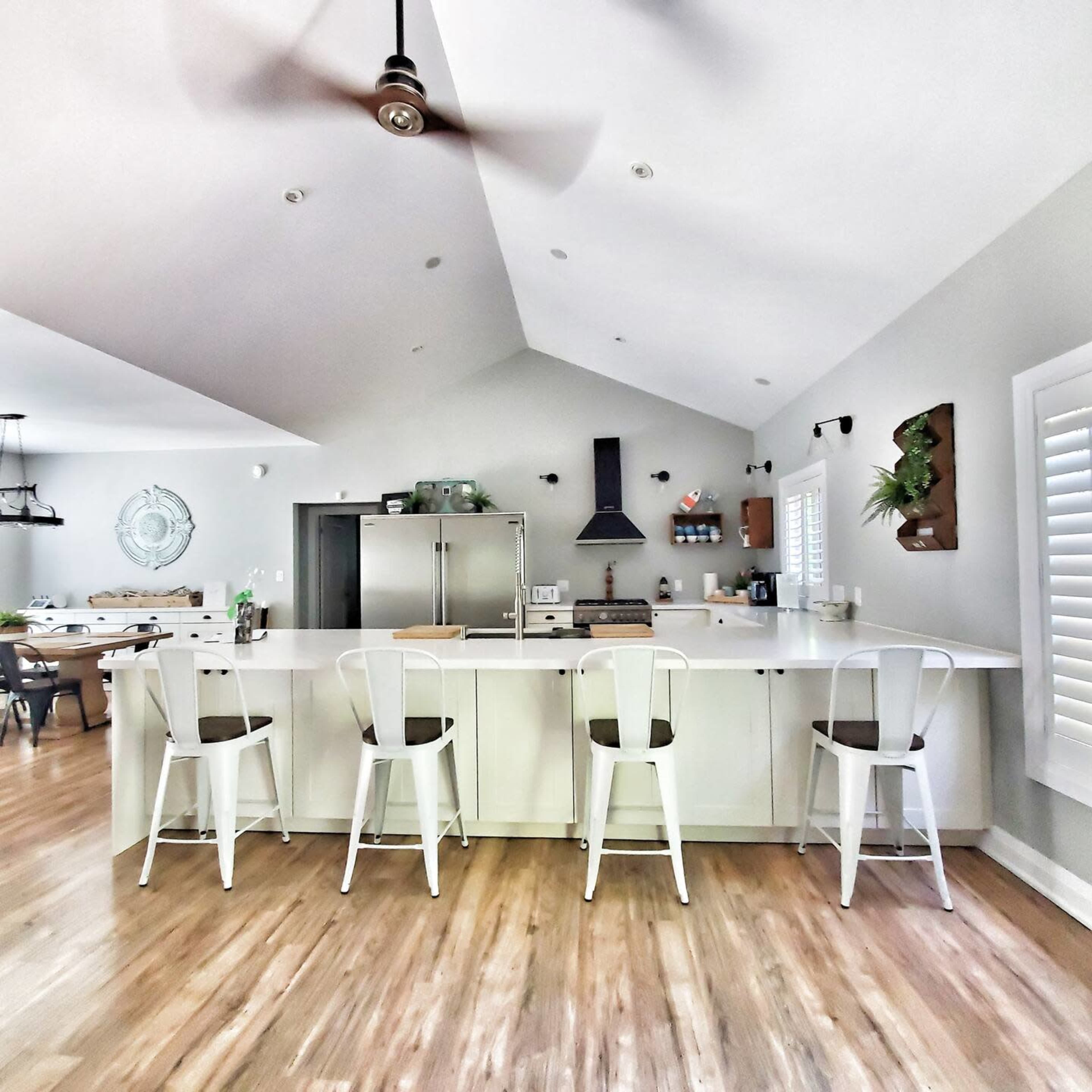 The image shows a modern kitchen with a large island, four bar stools, and a vaulted ceiling.