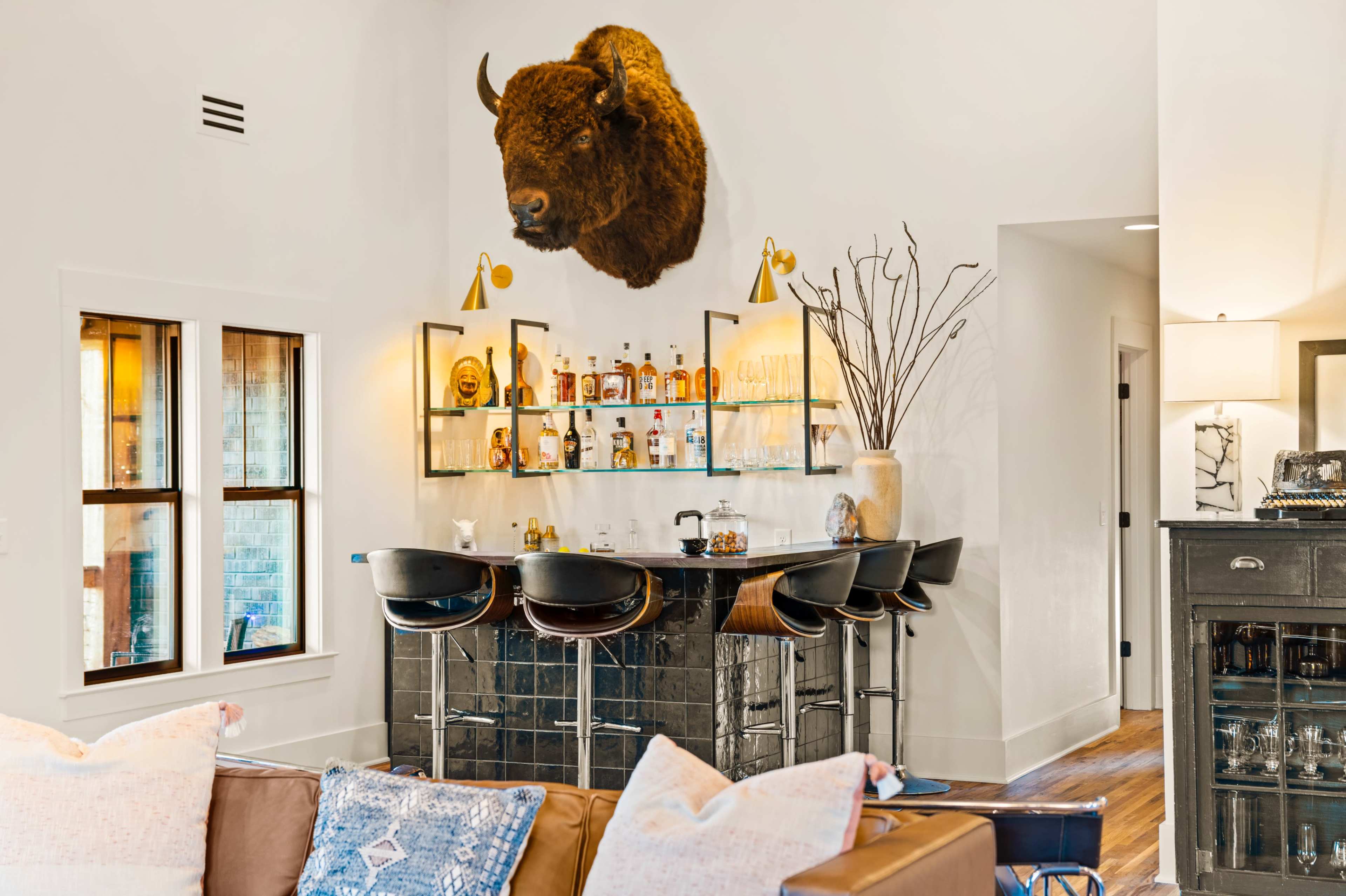 A mounted bison head is displayed above a glass bar with various bottles, situated in a well-lit, modern living area.