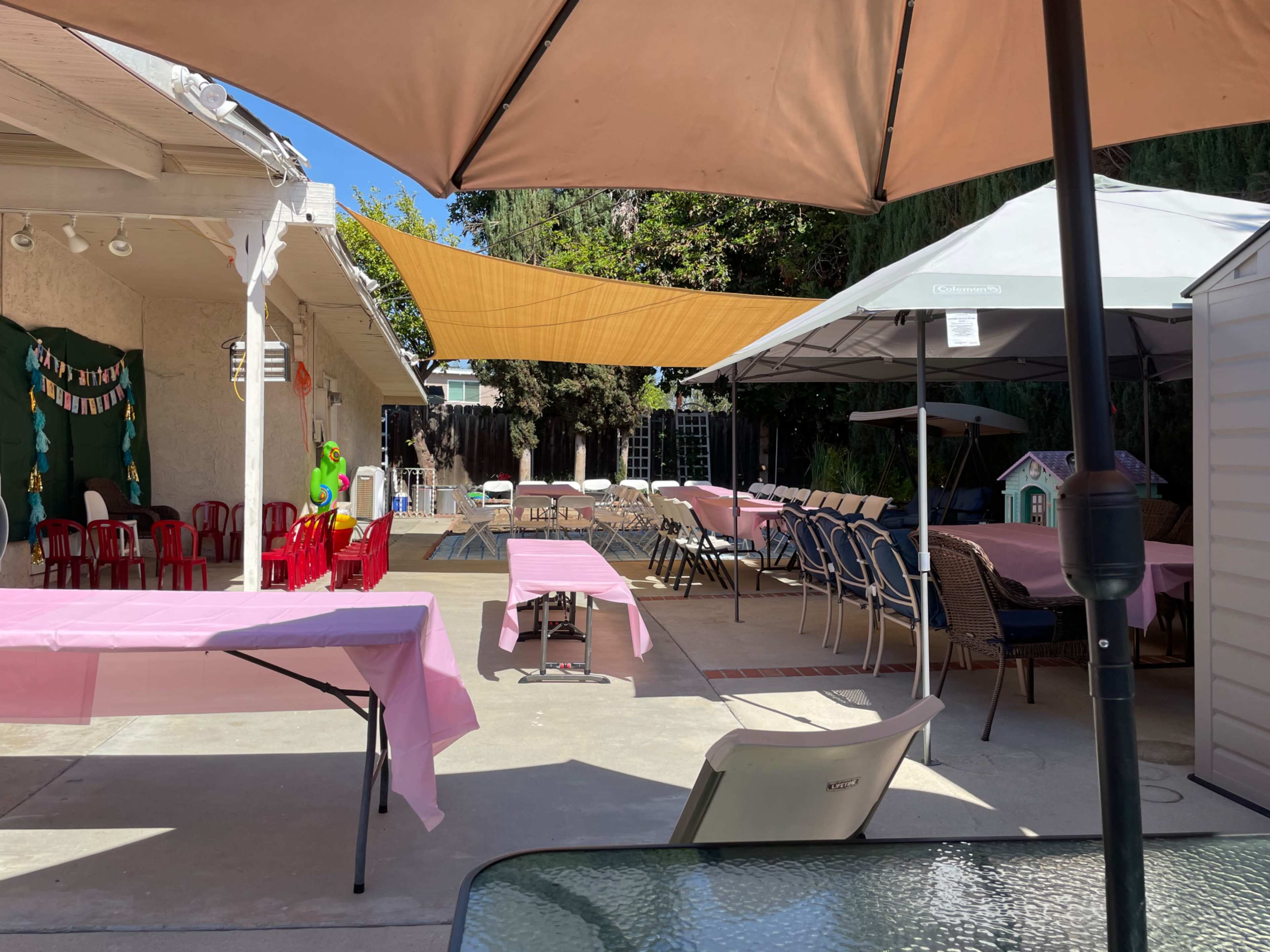 A decorated outdoor space features rows of tables and chairs under large umbrellas, with a swimming pool in the background.