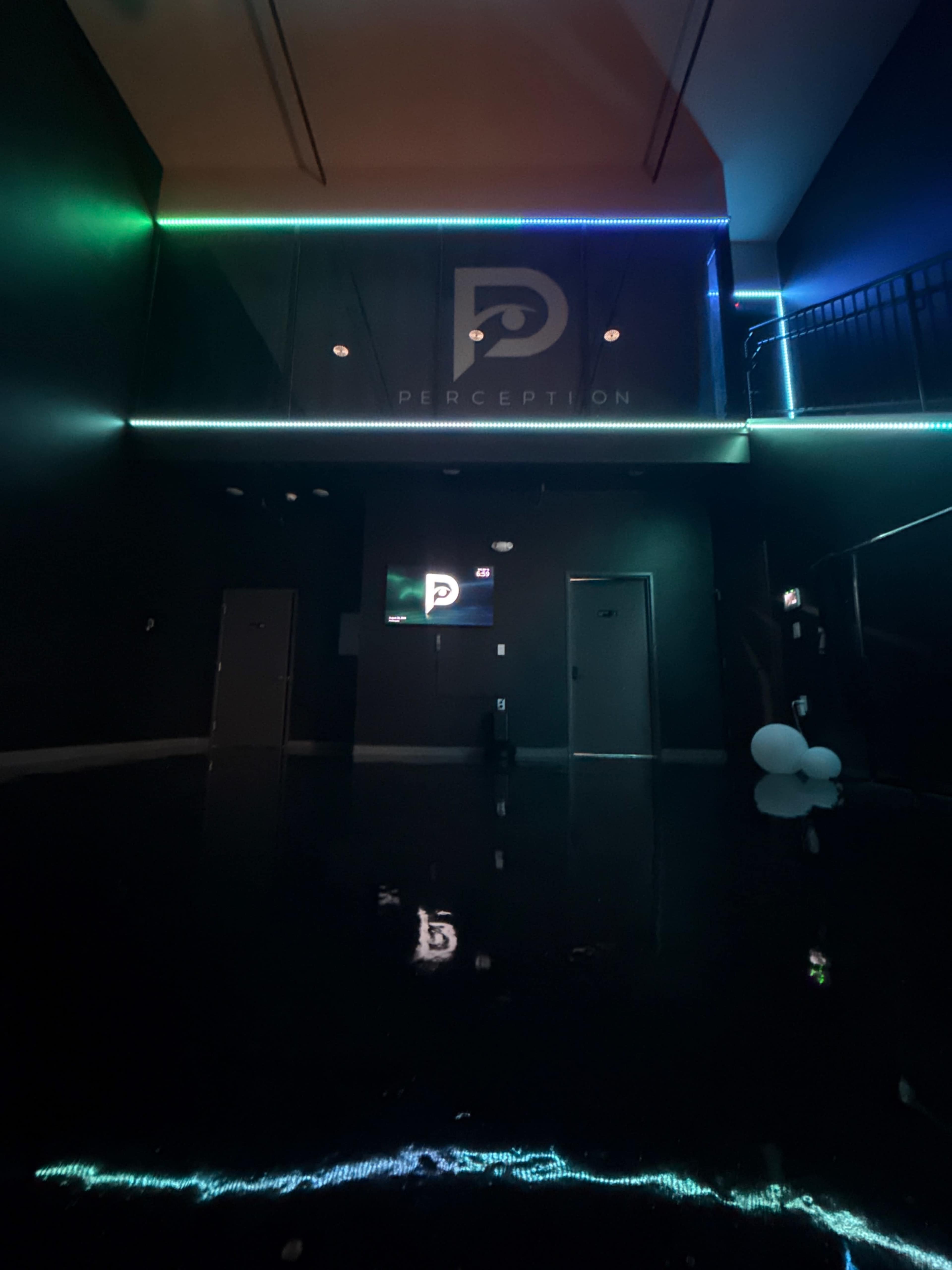 The image shows a dimly lit entrance area with a glossy floor and neon lights illuminating the walls, featuring the word "PERCEPTION" prominently displayed.