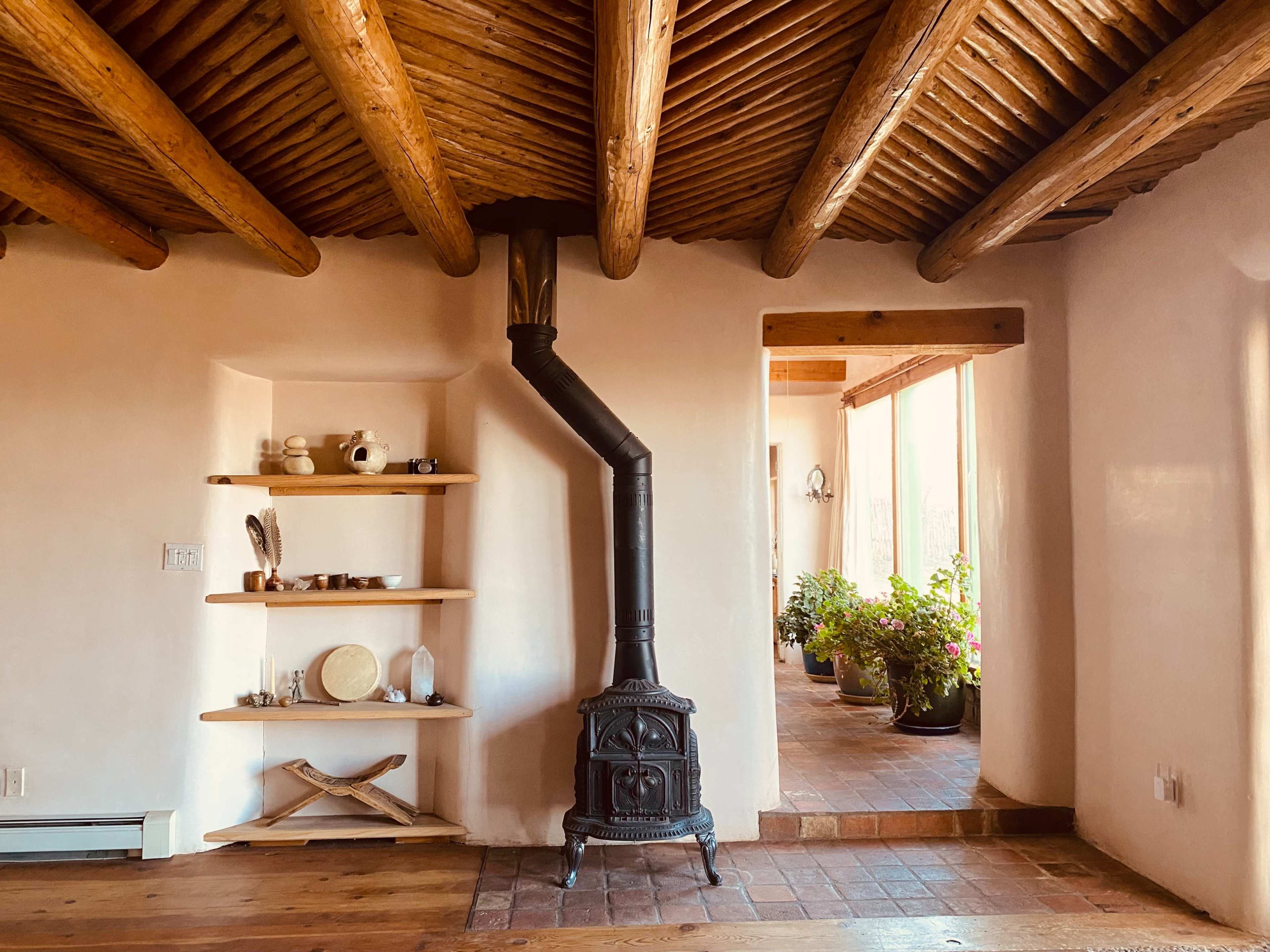 A rustic room with exposed wooden beams, a black stove, and shelves displaying various ceramic dishes and pots.