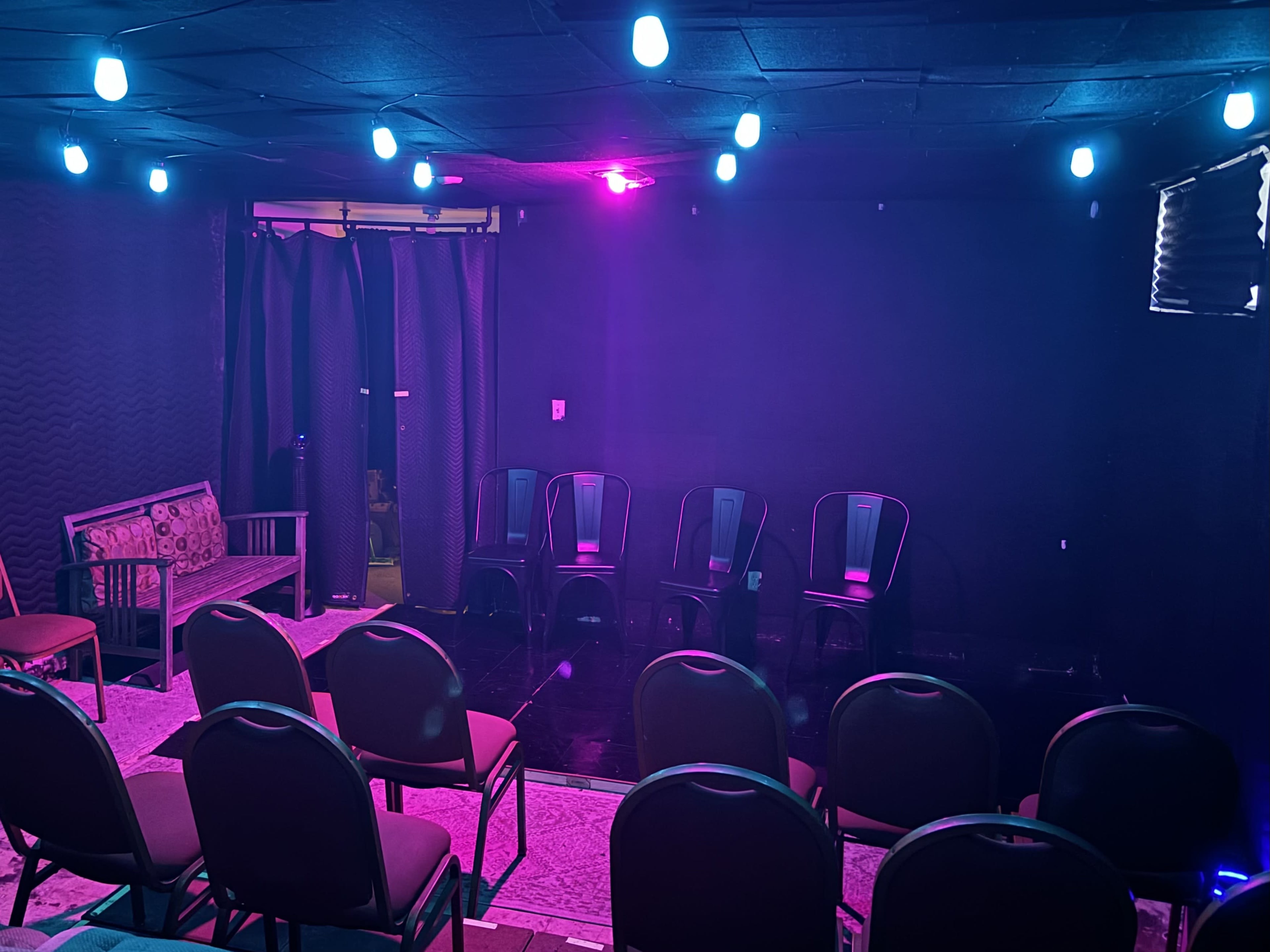 A dimly lit performance space with chairs arranged in rows facing a small stage area.