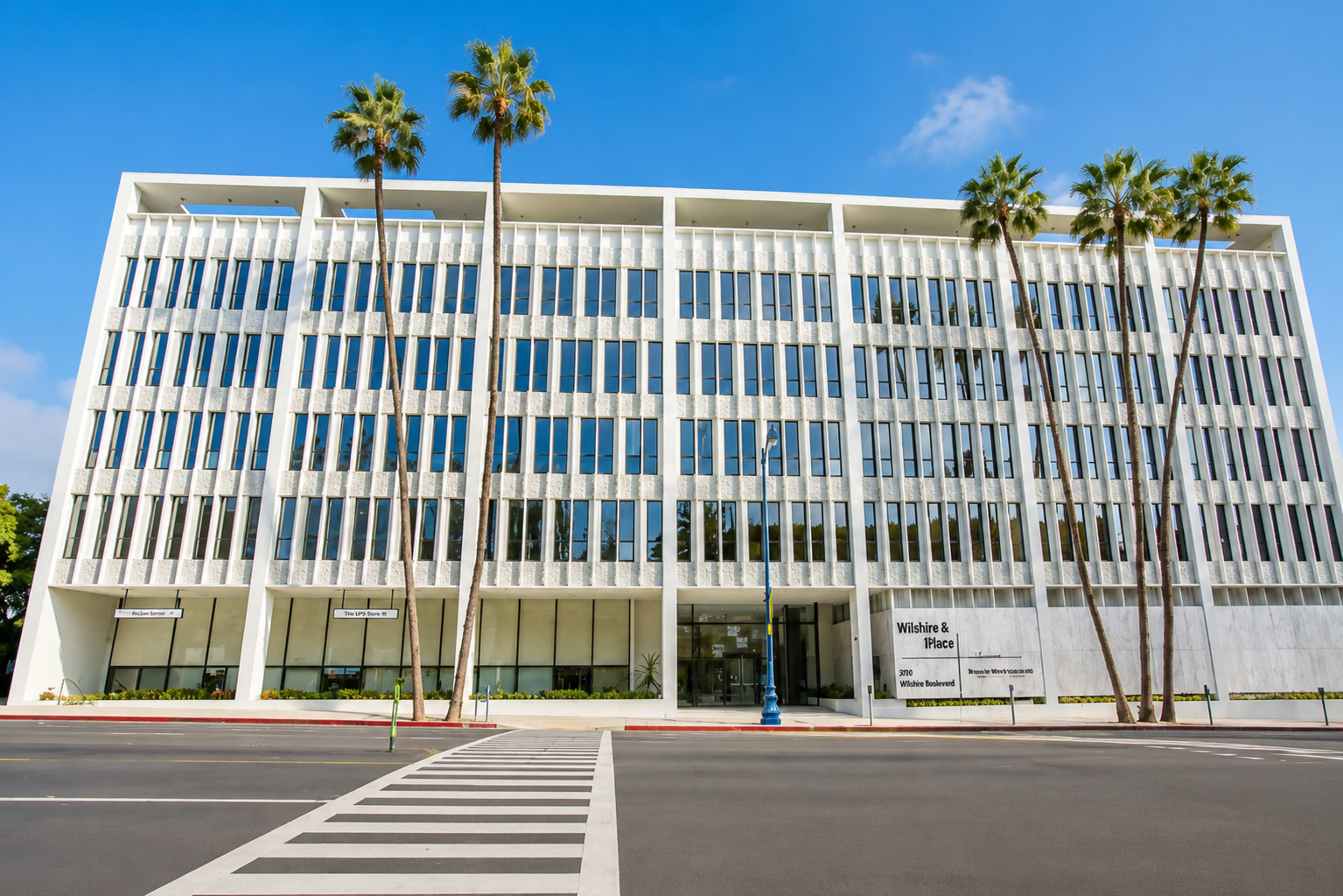 The image shows a modern, multi-story office building with large glass windows and palm trees in front, located alongside a street.