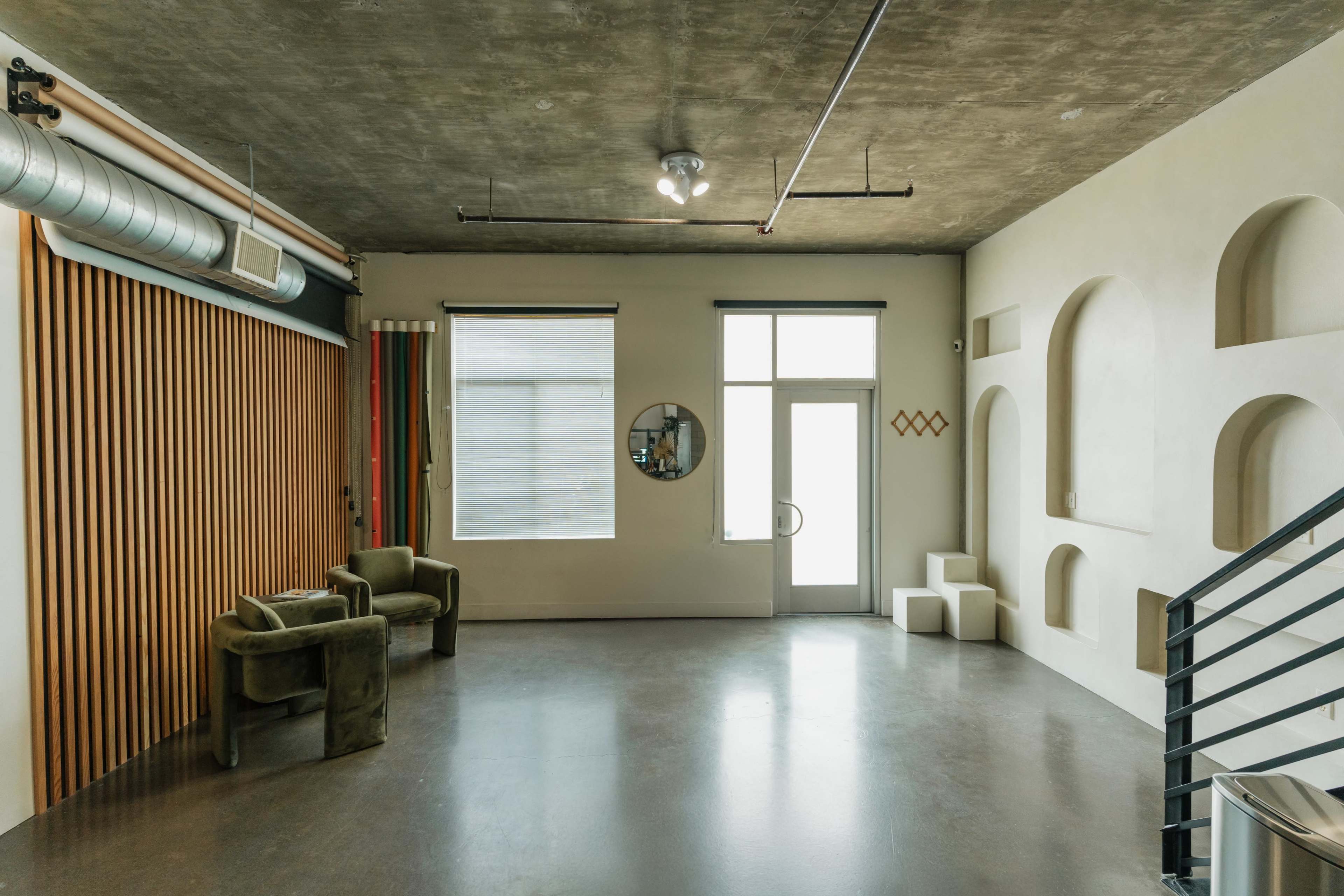 The image shows a minimalist interior space with a concrete ceiling, large windows, and a combination of wooden and geometric architectural features.
