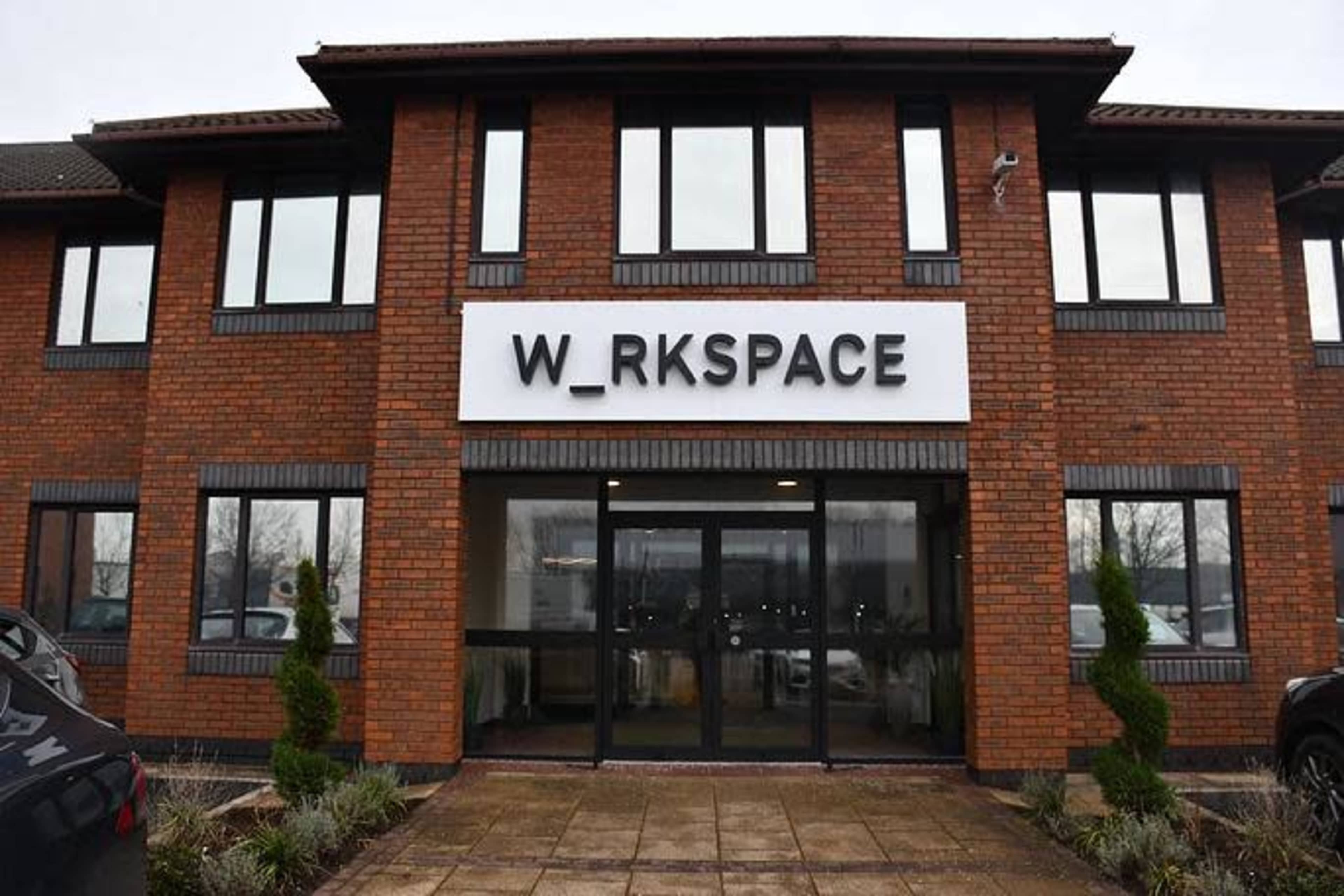 The image shows a modern brick building with a large sign reading "W_RKSPACE" above the entrance.