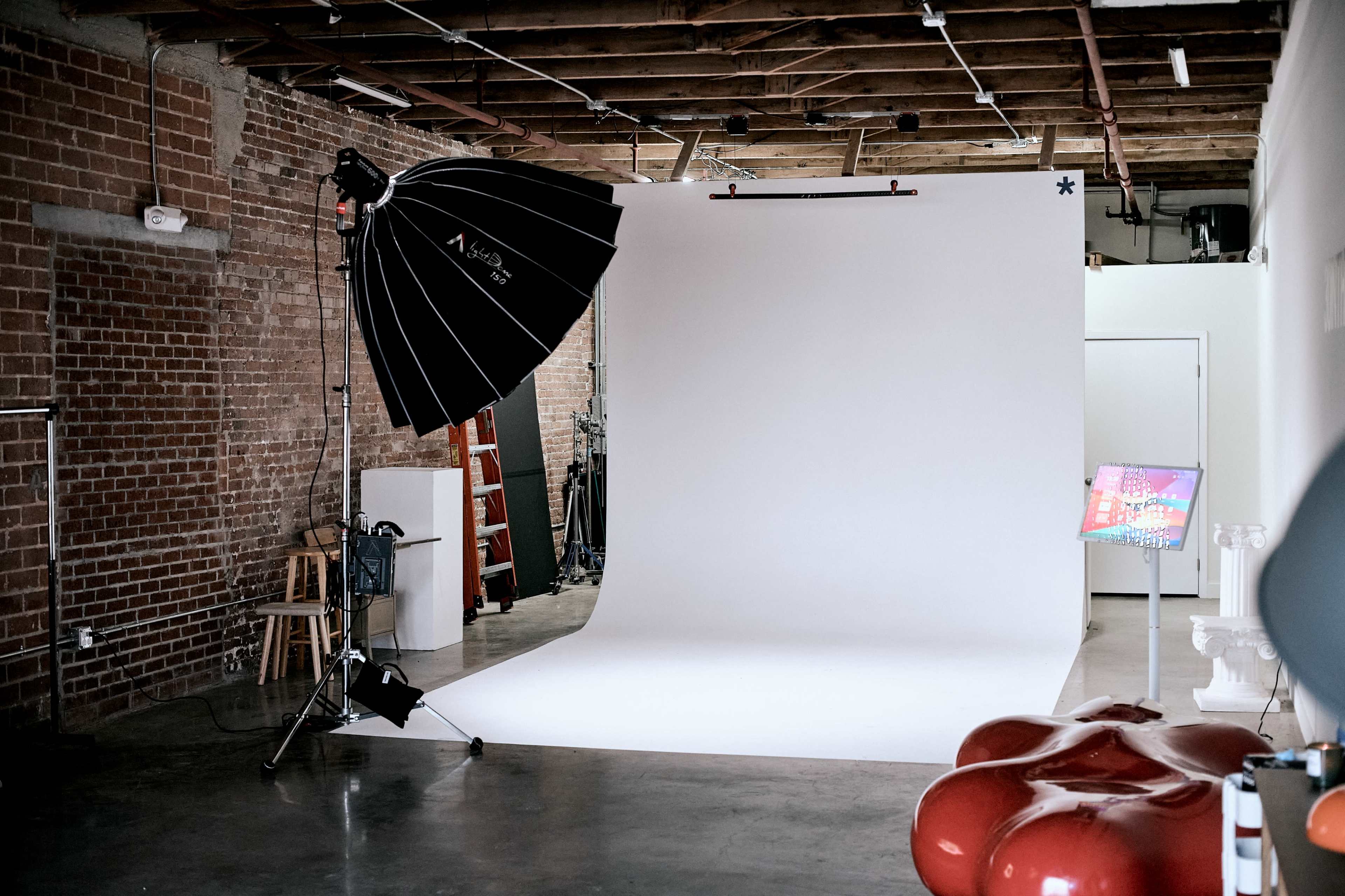 A photography studio features a large umbrella light, a white backdrop, and modern furniture in a spacious, industrial setting.