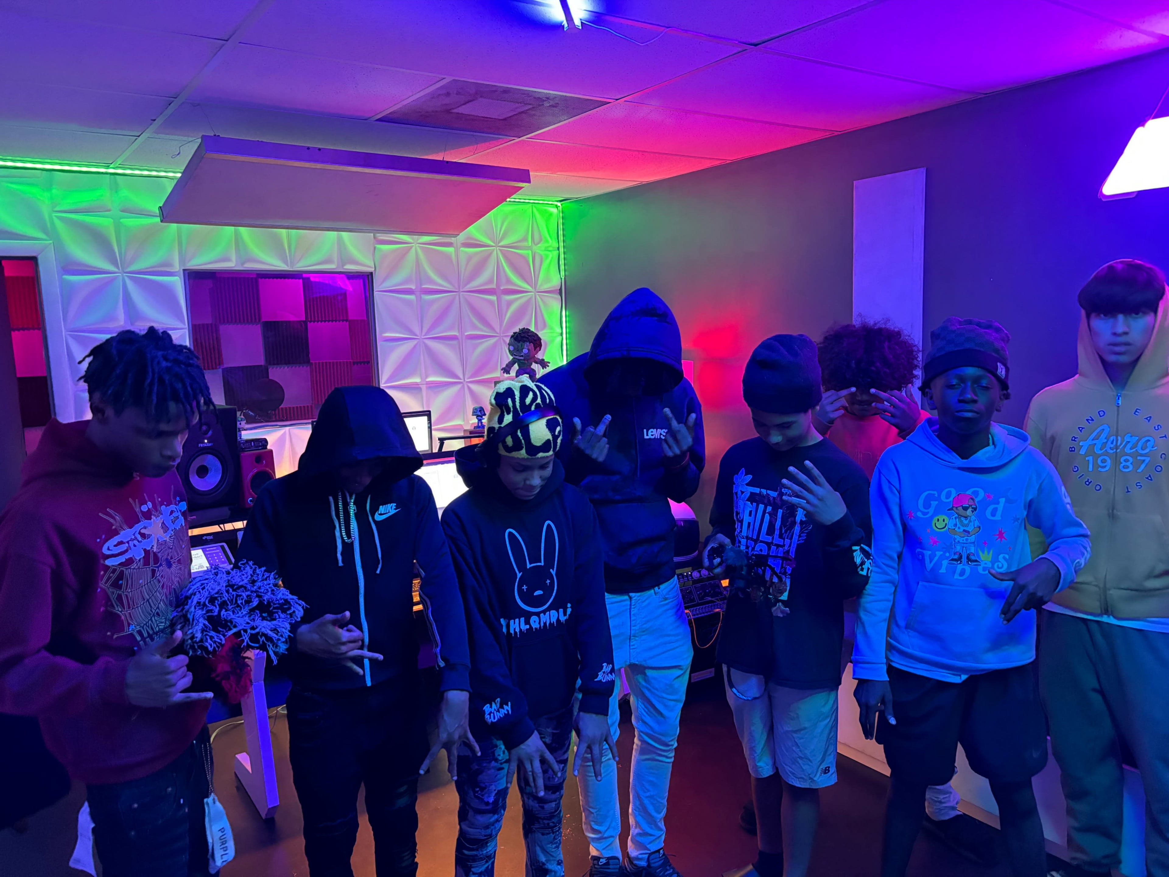 A group of young individuals stands together in a colorful studio environment with various lighting effects.