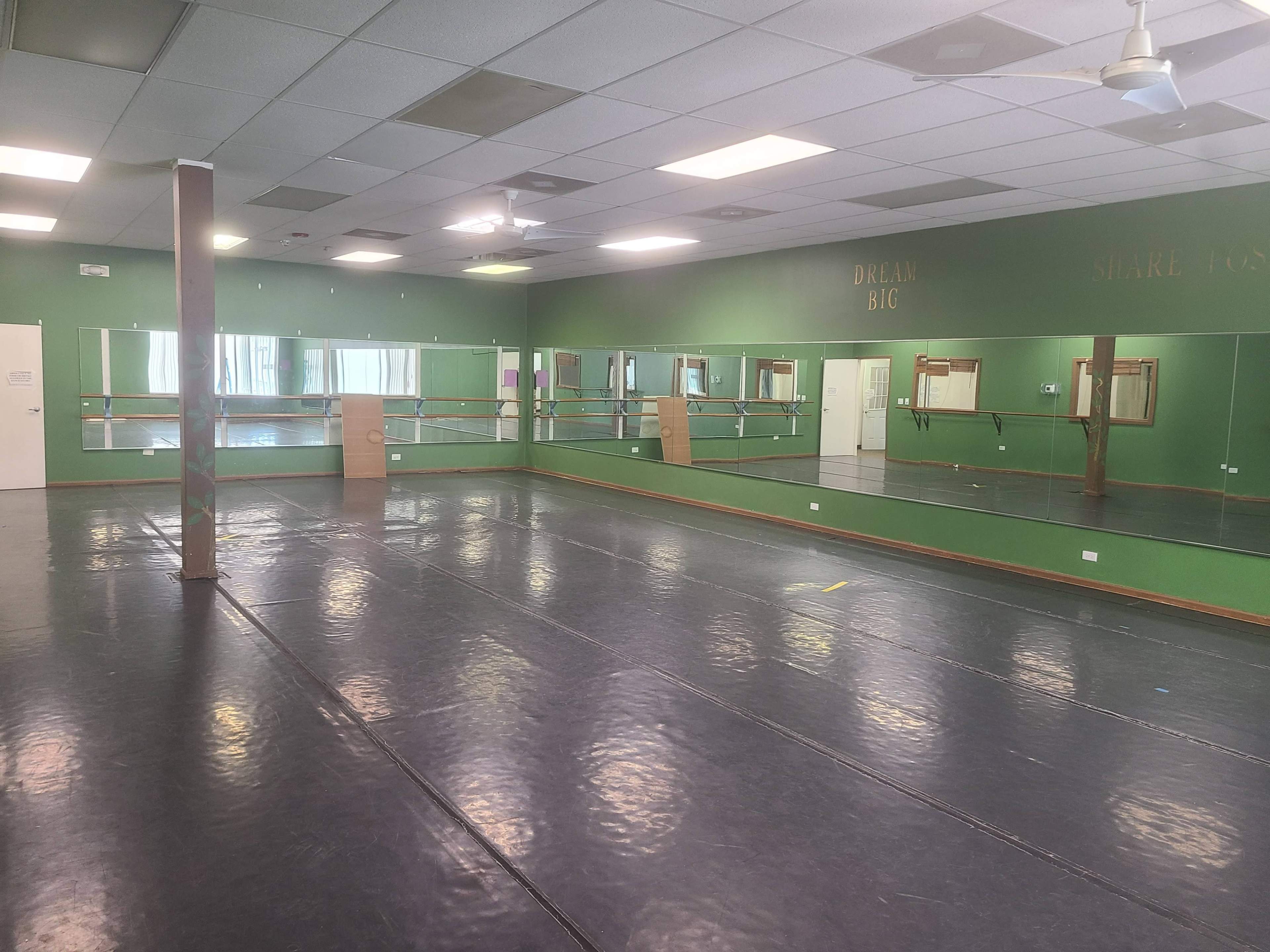 A spacious dance studio with mirrored walls, a wood barre, and a gray floor.