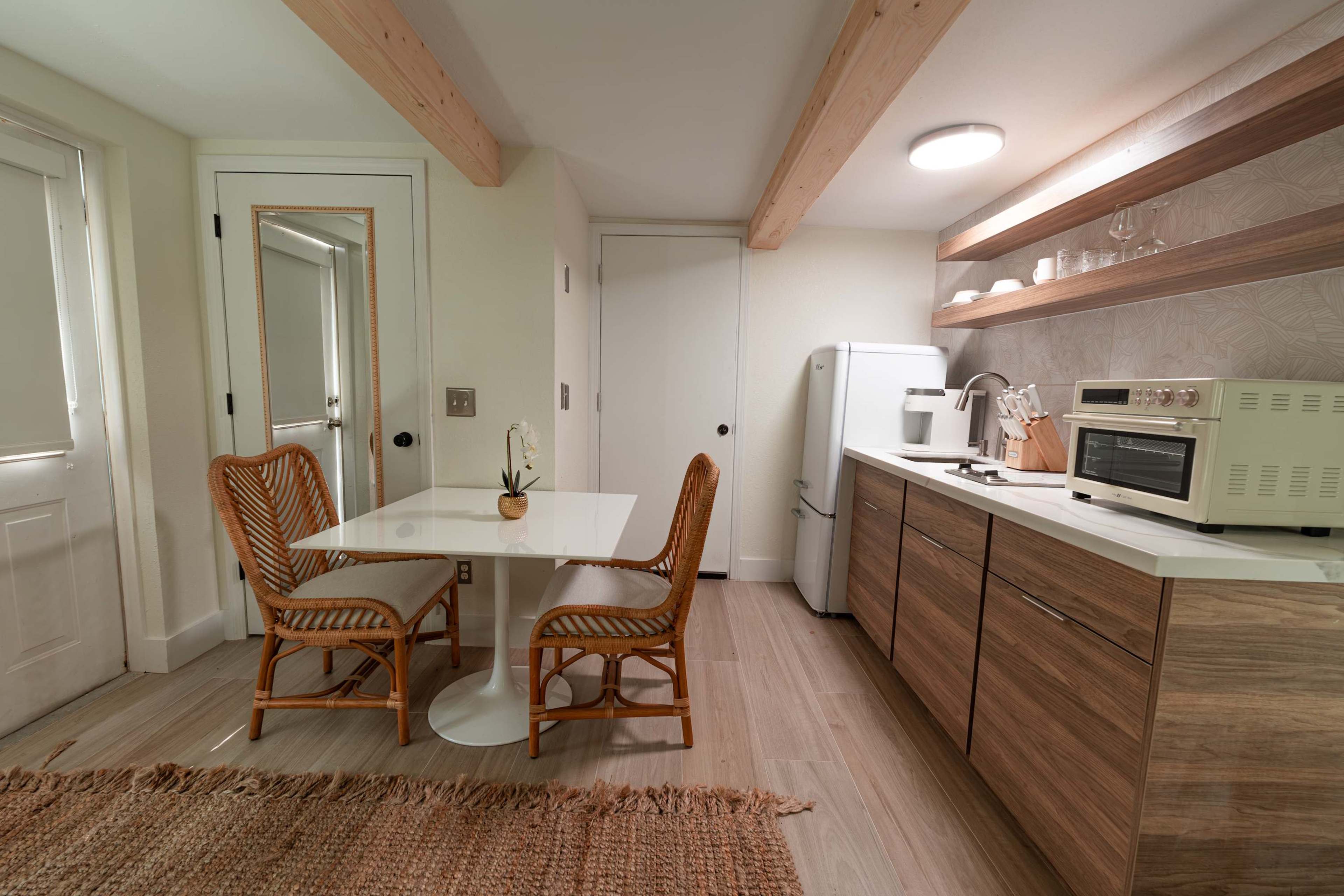 A modern kitchen features a round table with rattan chairs, a refrigerator, an oven, and wooden cabinetry, all illuminated by overhead lighting.