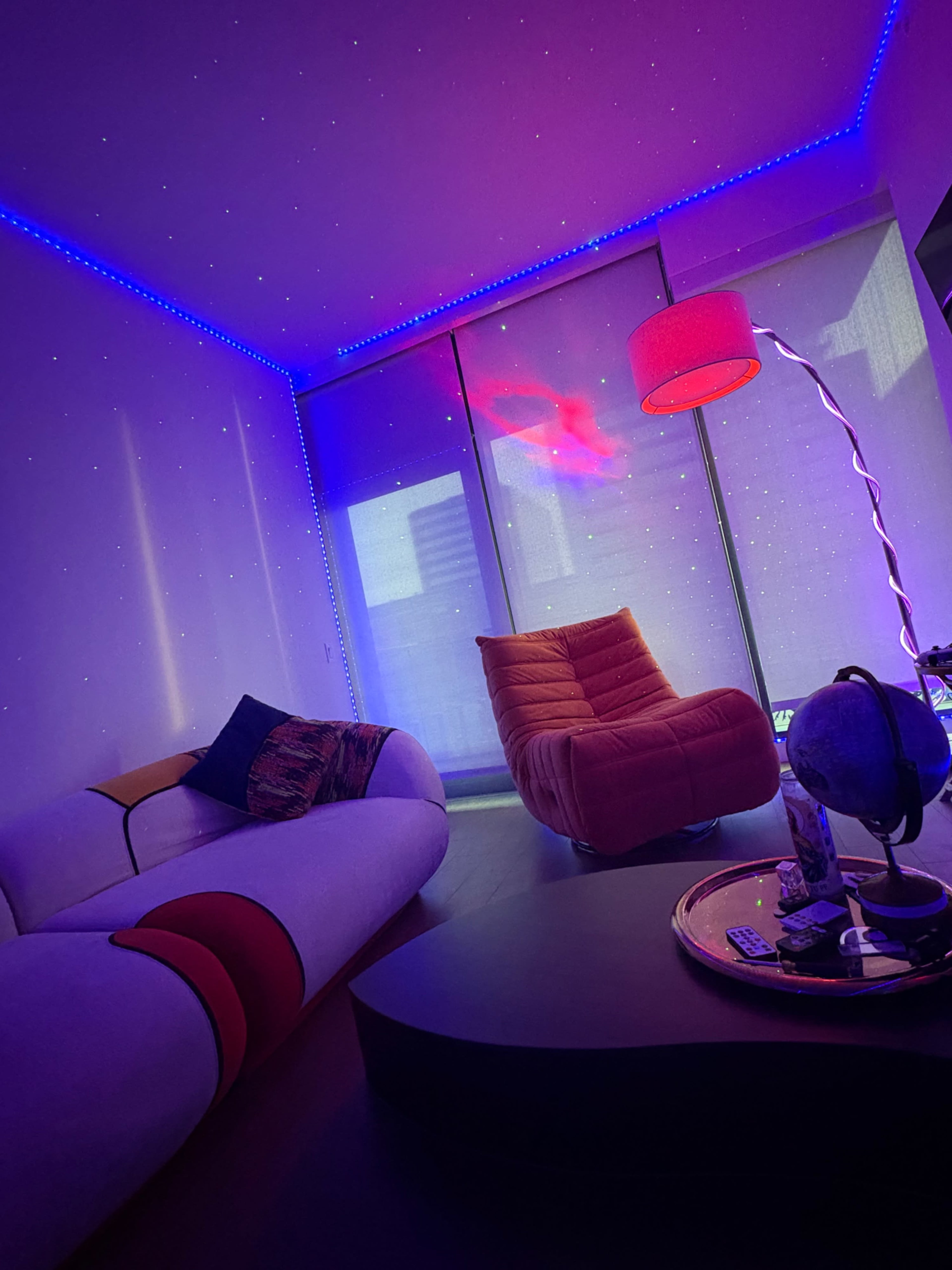 A modern living room features a curved couch and a red chair illuminated by colorful LED lights.
