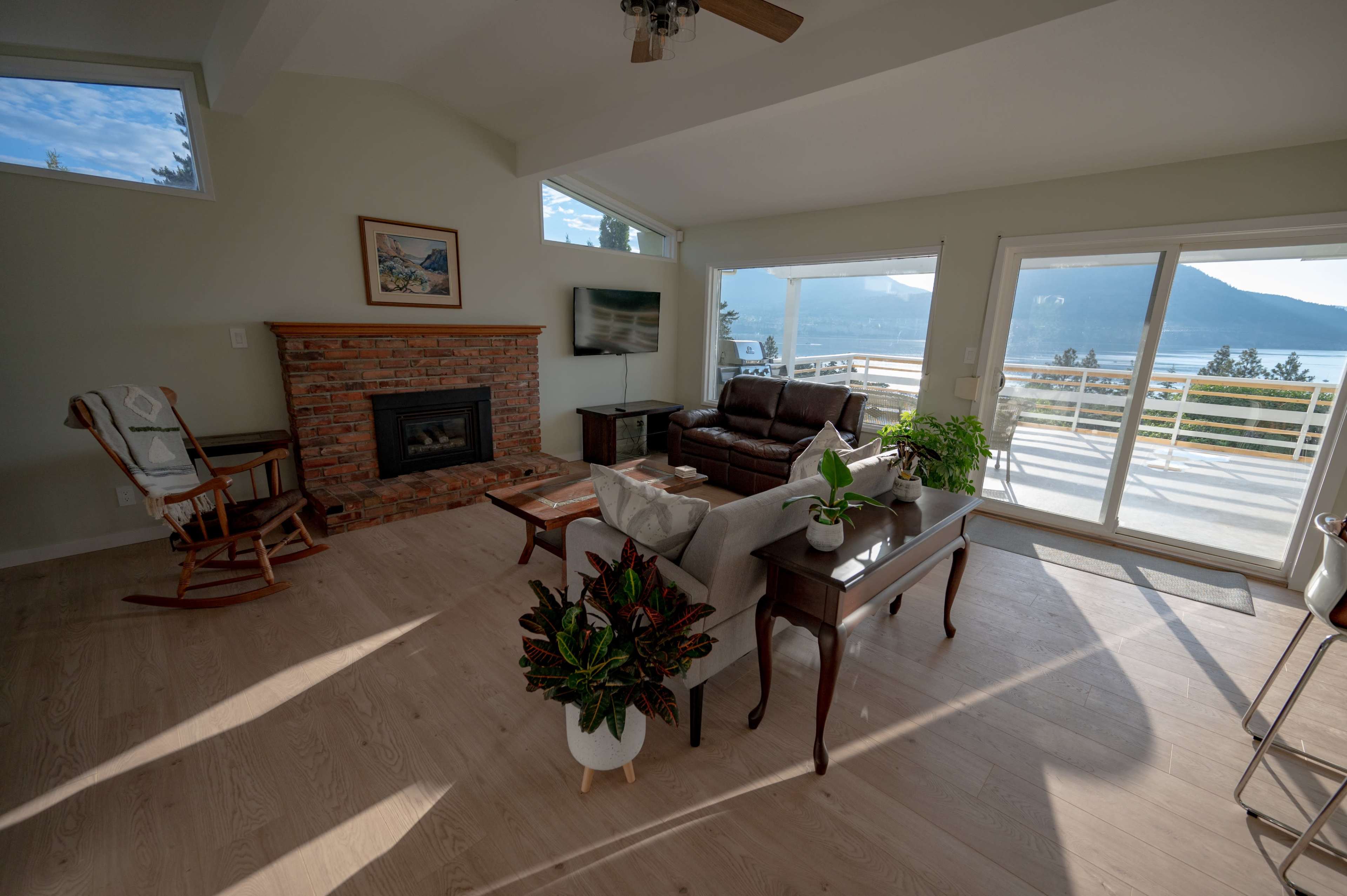 A bright living room with a fireplace, a couch, and large windows offering a view of the outdoors.