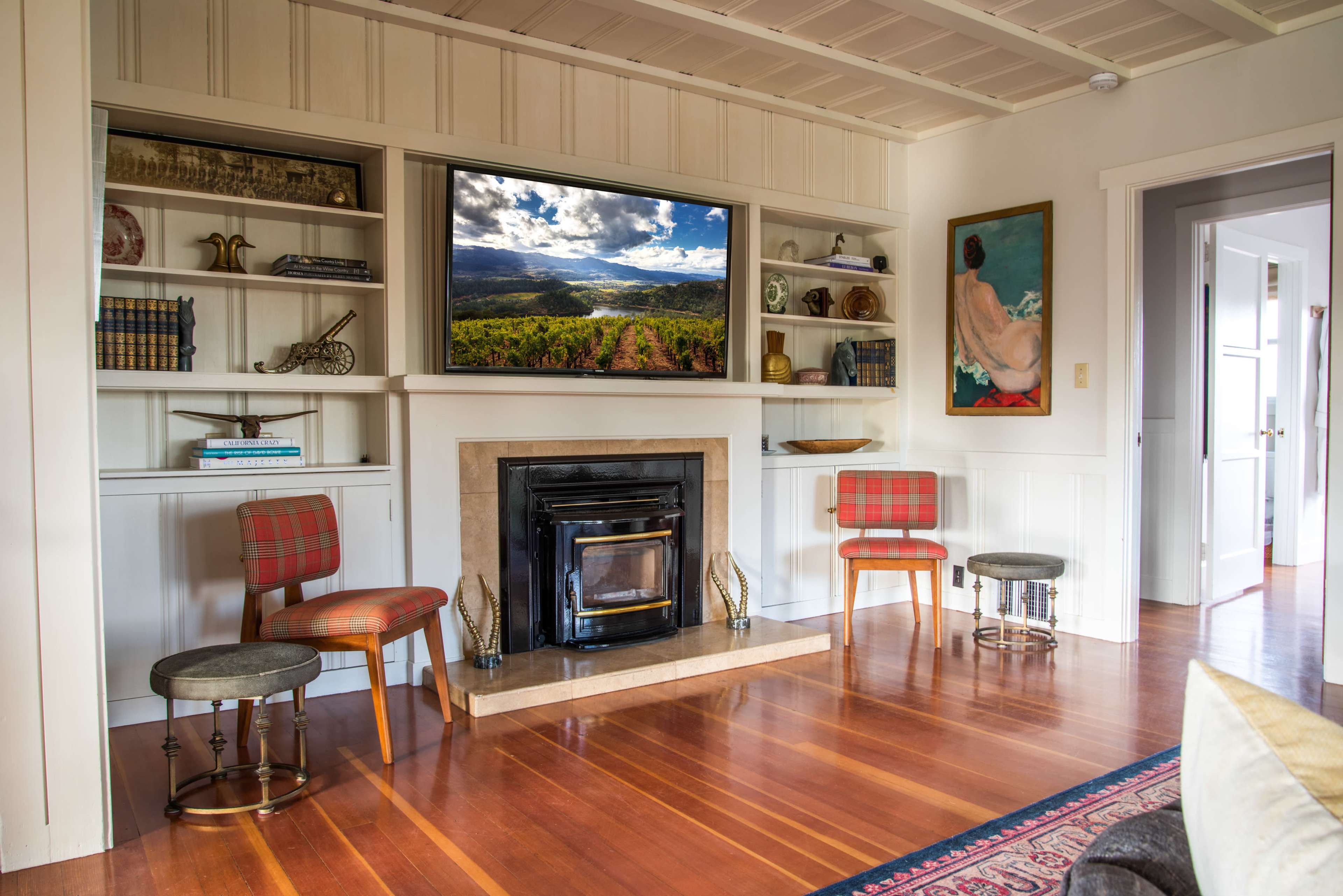 The room features a modern fireplace with a television mounted above it, surrounded by built-in shelves displaying books and decor, with two upholstered chairs and a rug on polished wooden flooring.