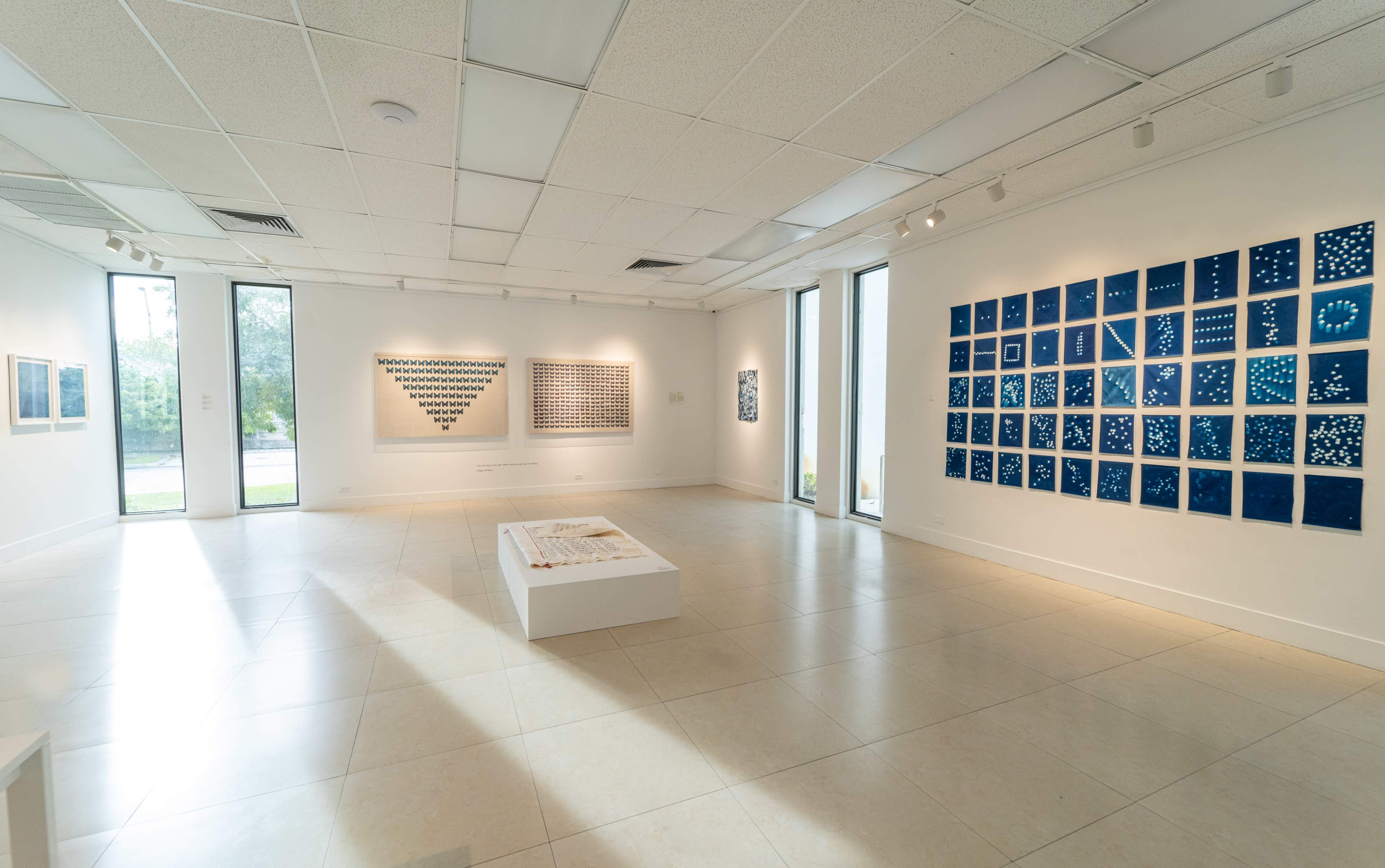 An art gallery featuring a spacious layout with blue and white artworks displayed on the walls and a central white exhibit on the floor.