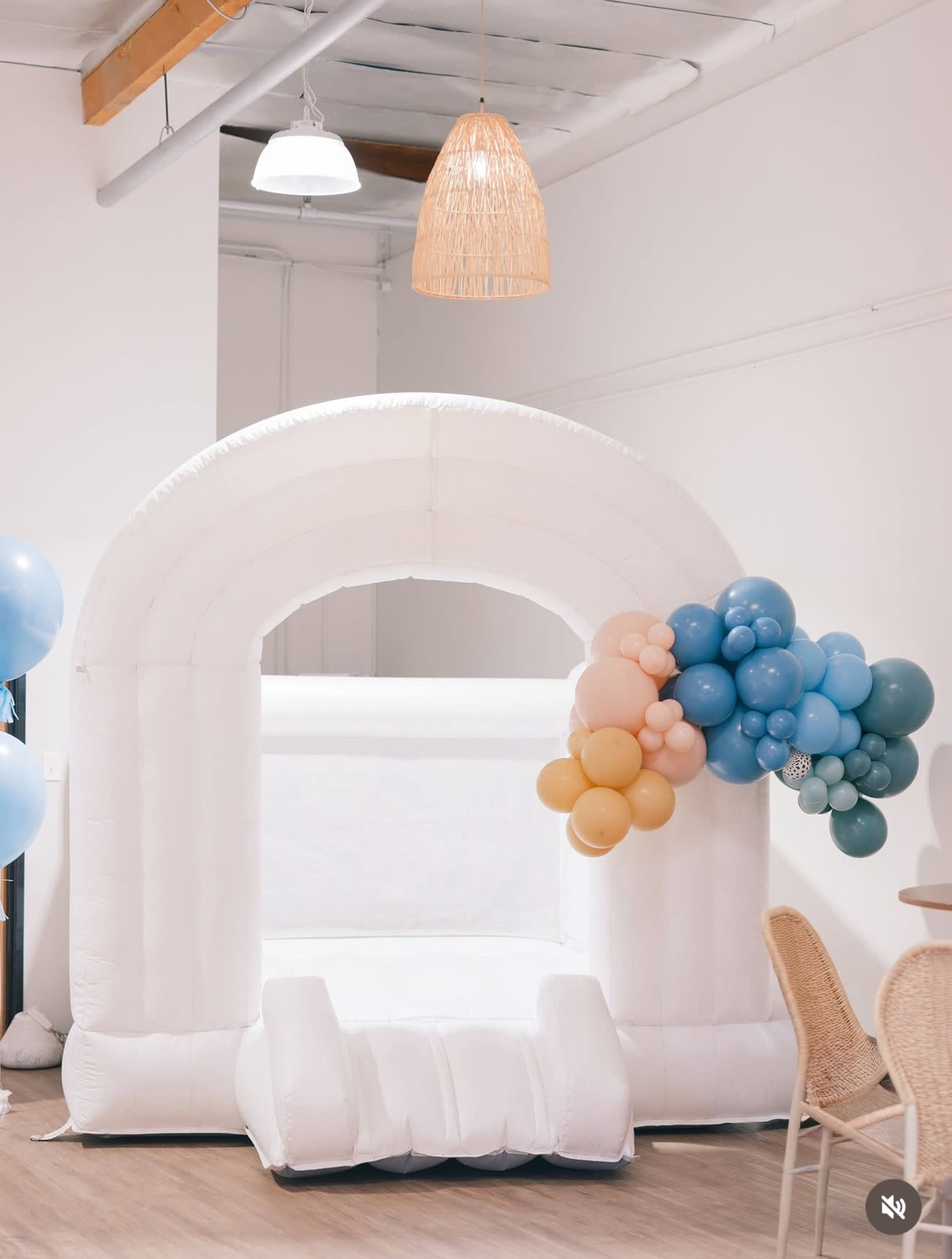 A large white inflatable bounce house is set up indoors, adorned with a cluster of colorful balloons at one corner.