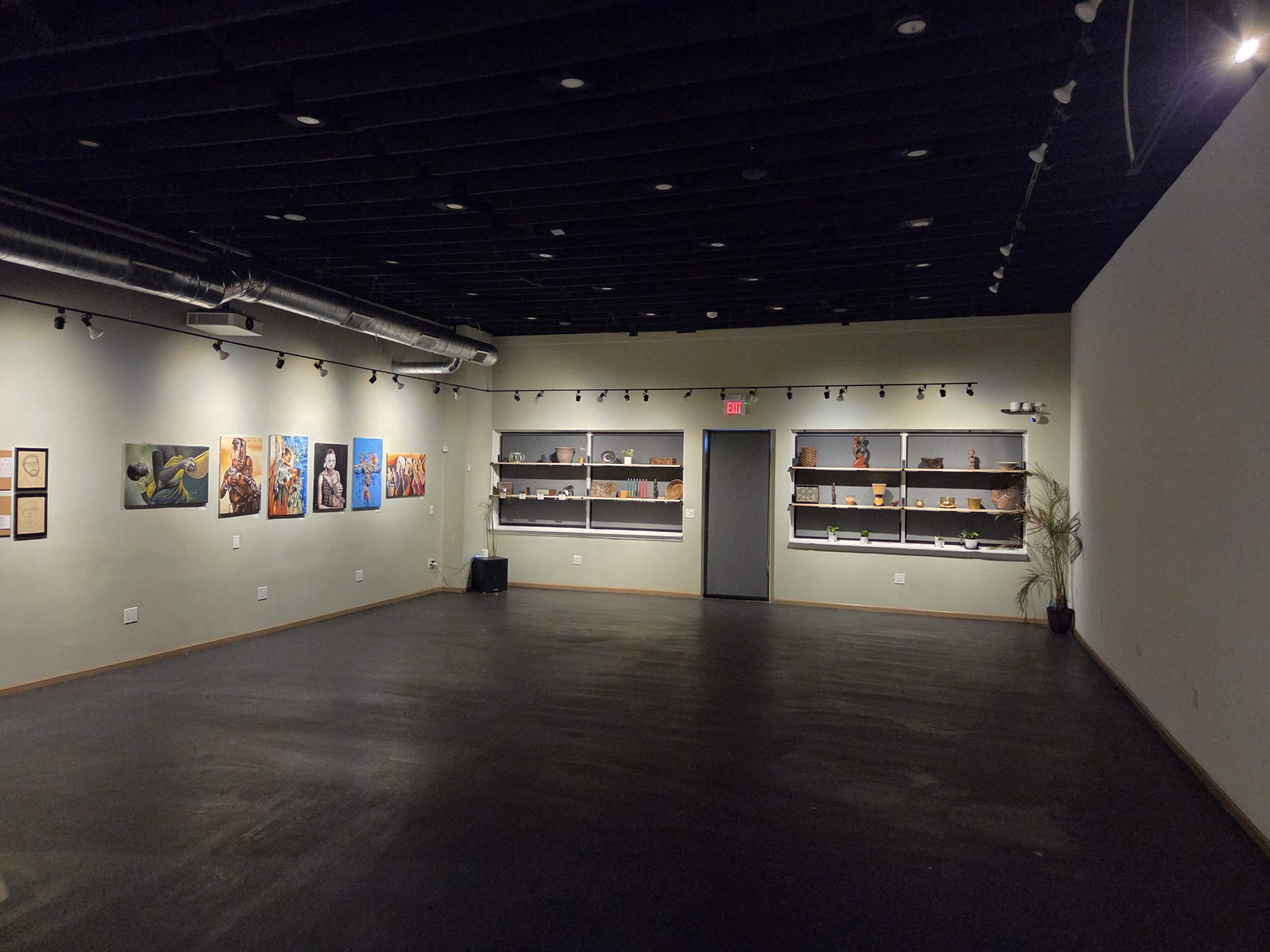 The image shows an art gallery with several paintings on the left wall and shelves displaying sculptures and art pieces on the right side, all in a spacious, dimly lit room.