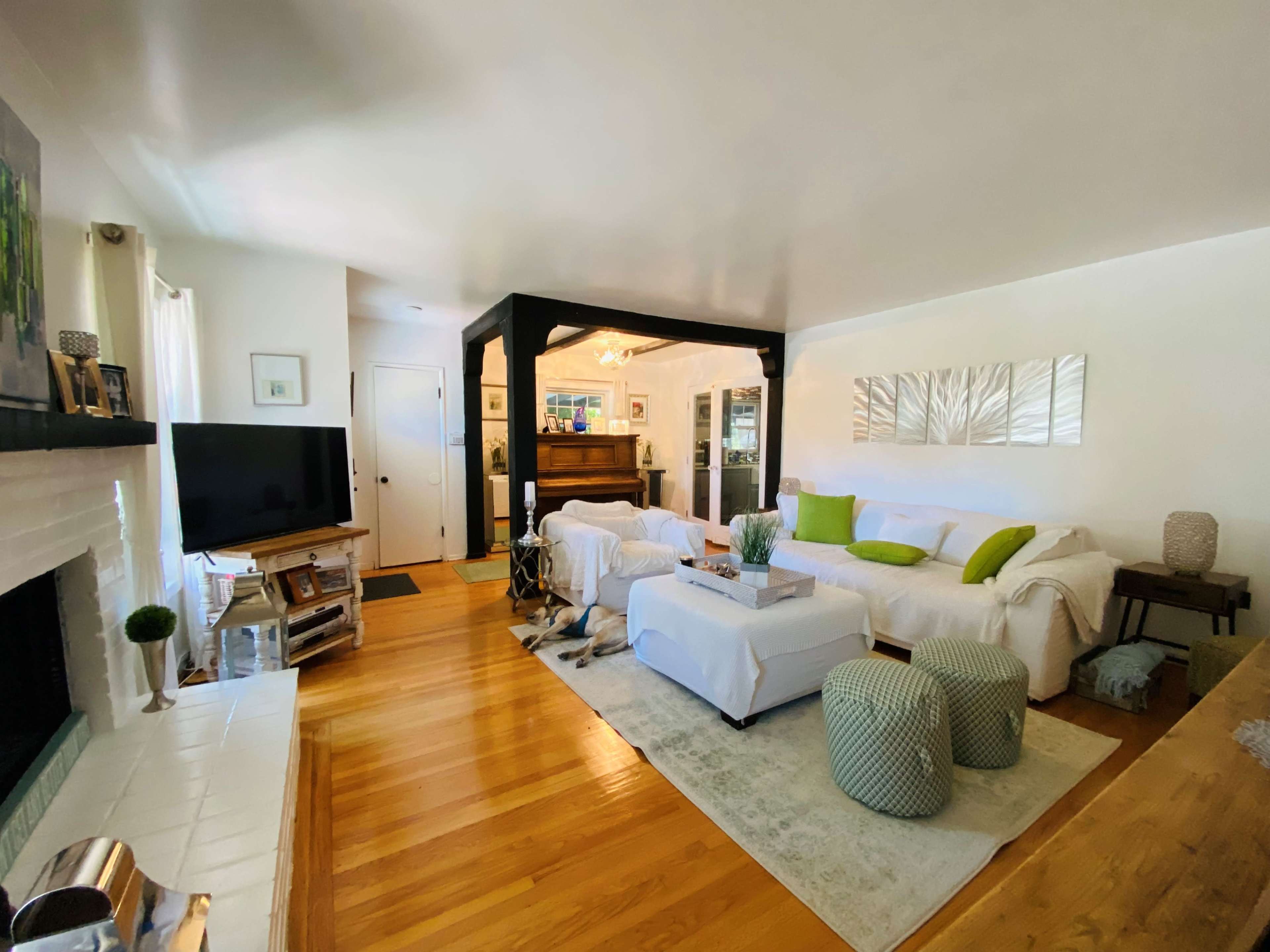 A bright living room with a white sofa, a coffee table, and a piano in the background, situated on wooden flooring.