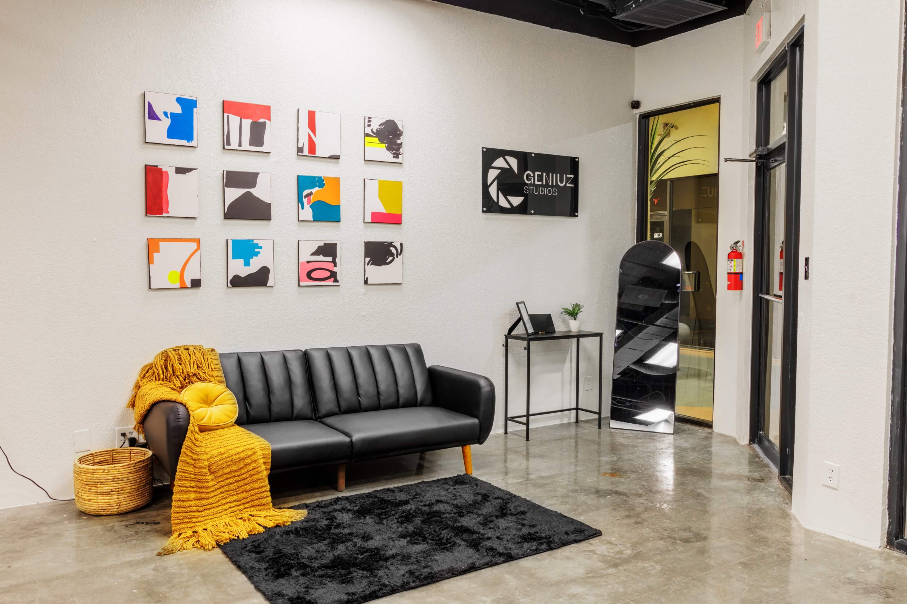 A modern lobby area with a black sofa, a yellow throw blanket, a textured black rug, and abstract art on the wall, along with a sign for "GENIUZ STUDIO."