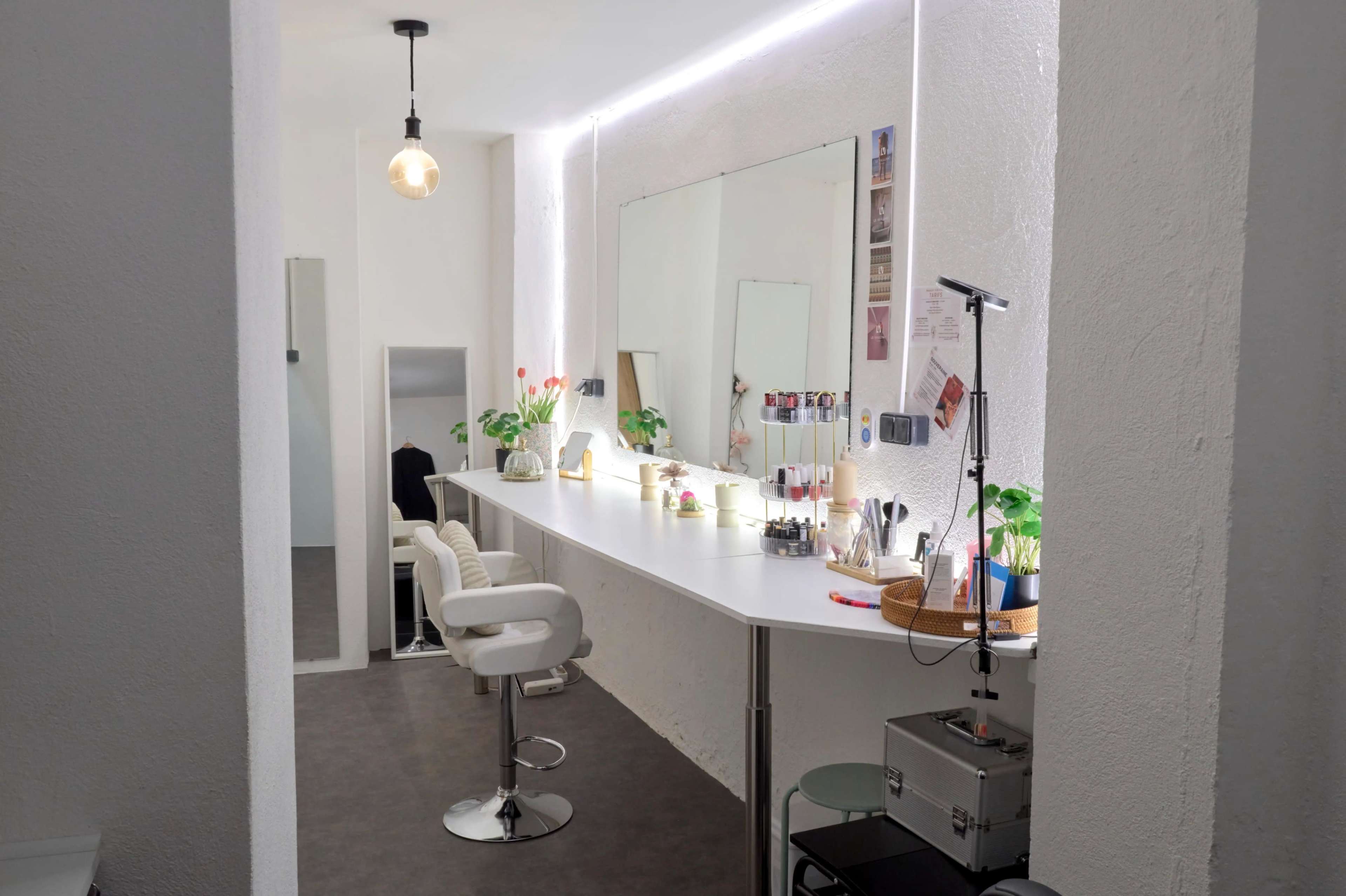 The image shows a modern beauty salon with a long vanity mirror, bar-style seating, and plants arranged on a sleek counter.