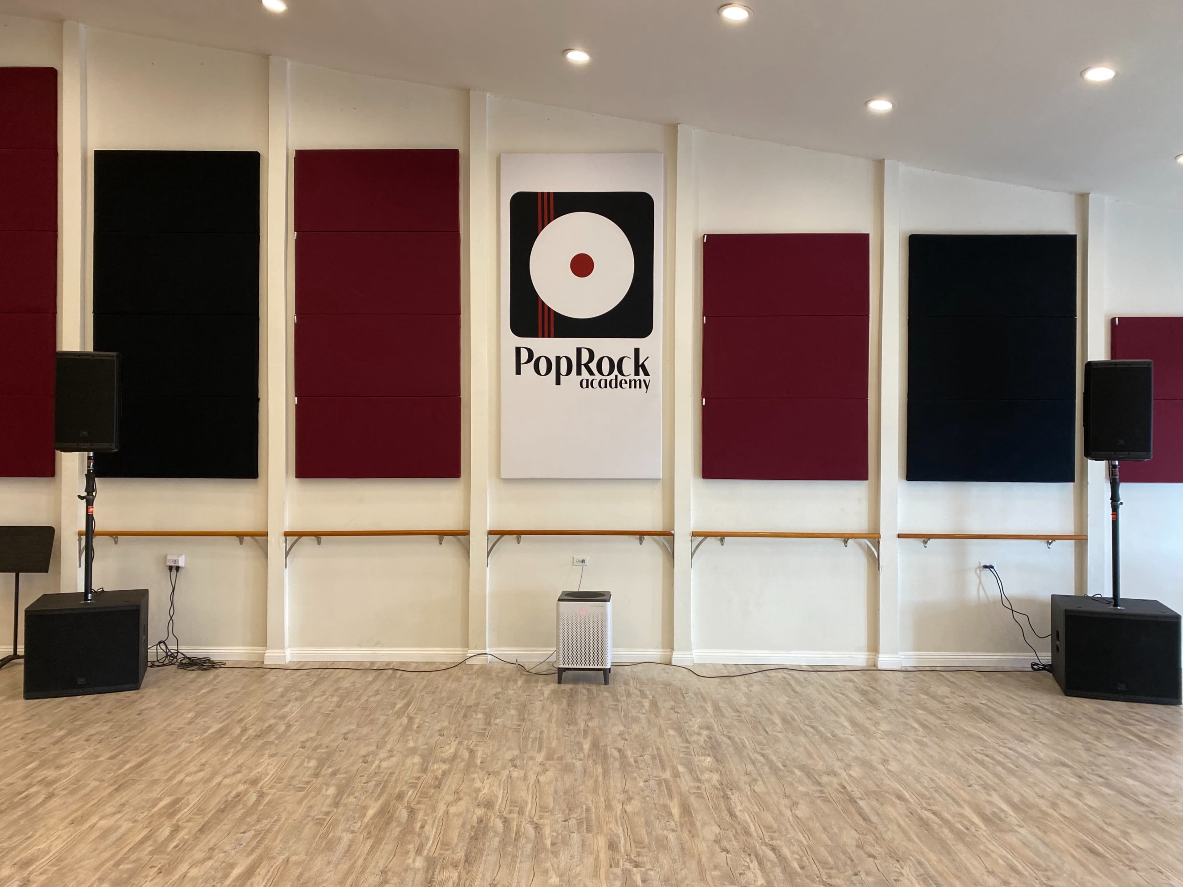 A music studio with soundproof panels on the walls, featuring the logo of "PopRock Academy" in the center.