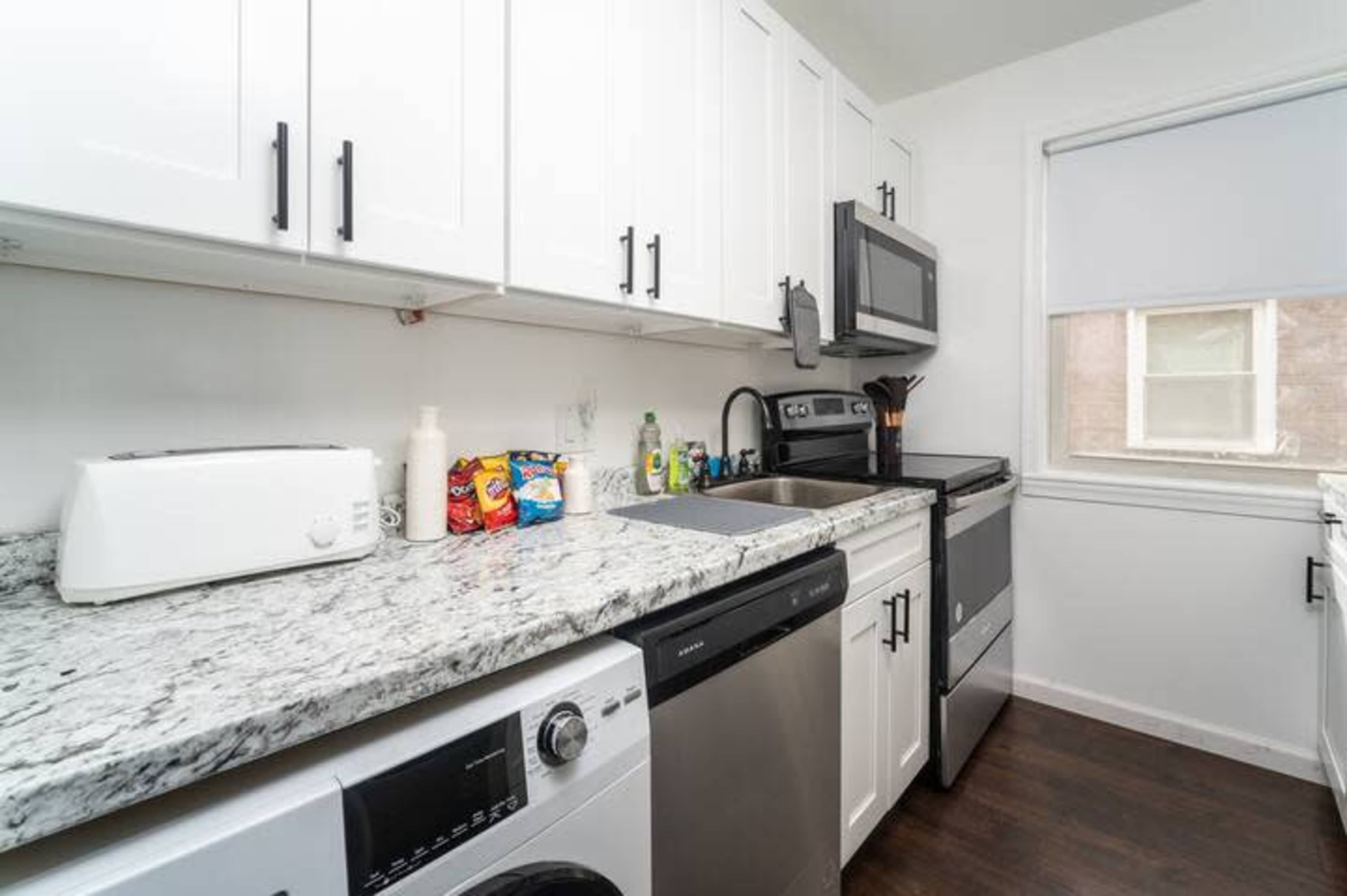 A modern kitchen features white cabinetry, stainless steel appliances, and a granite countertop, with a washing machine and dryer included.