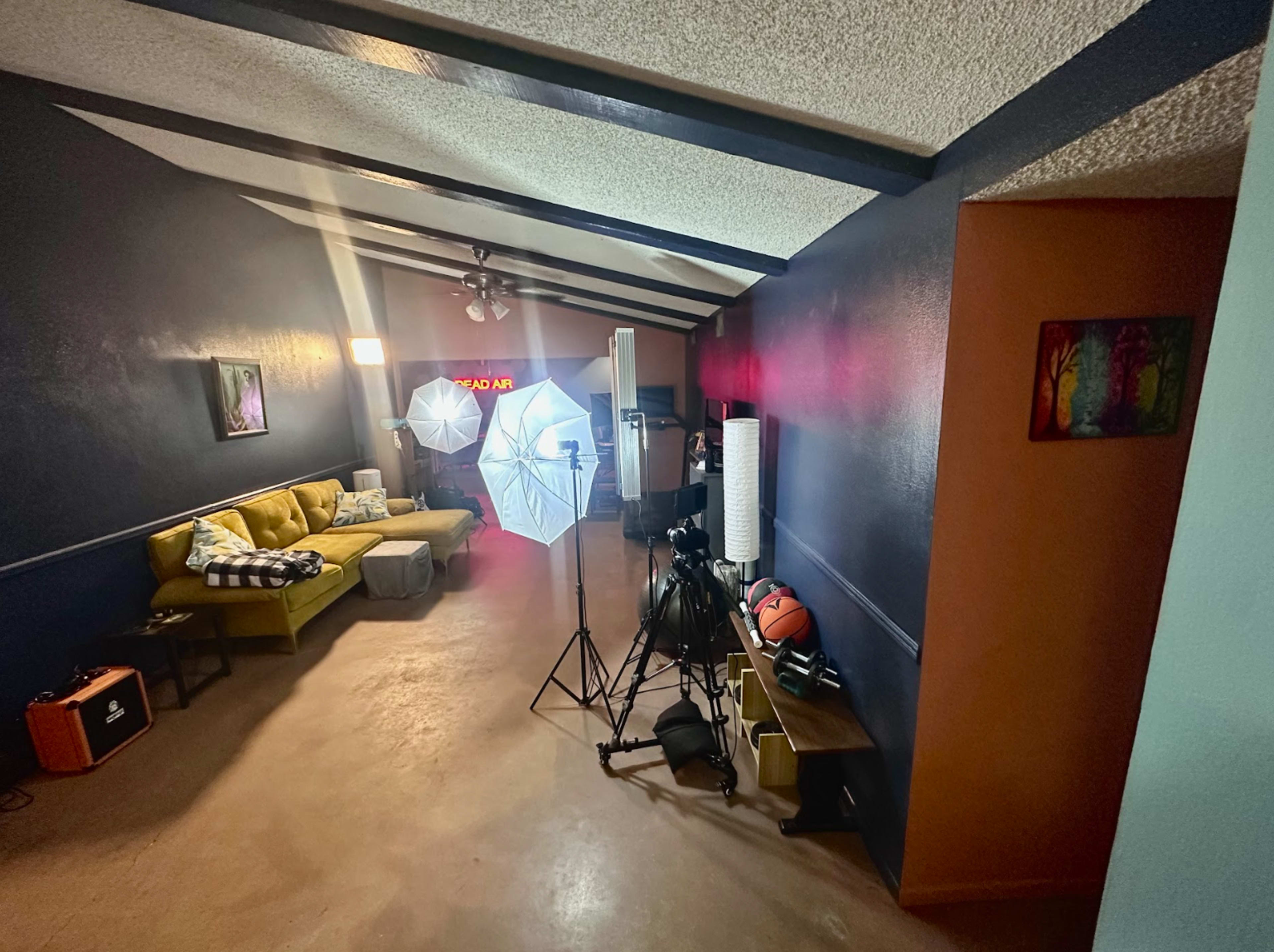 The image shows a spacious room with a green couch, photography equipment, and soft lighting from multiple sources.