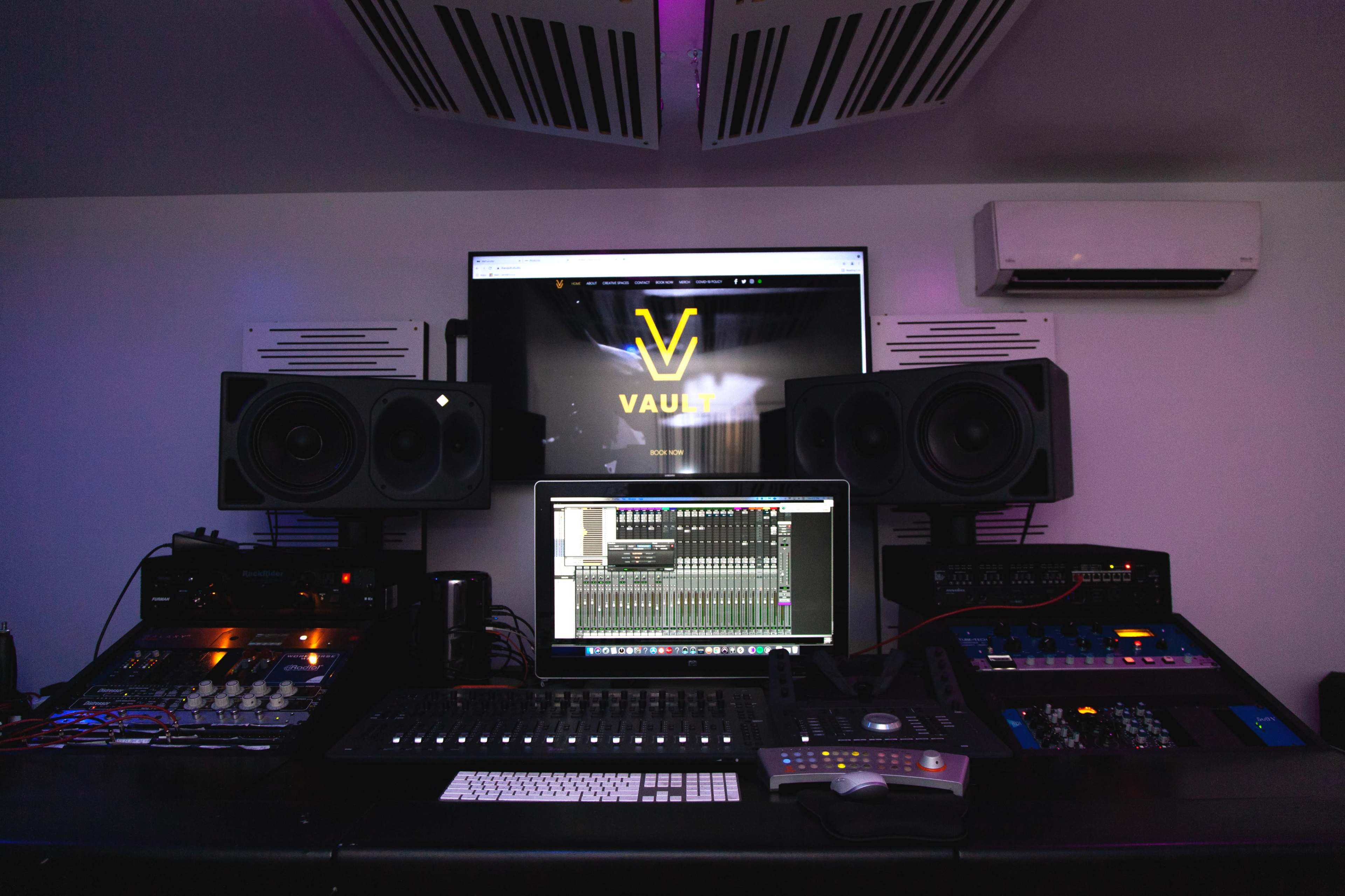 A music production studio with a computer displaying audio software, large studio monitors, and various audio equipment.