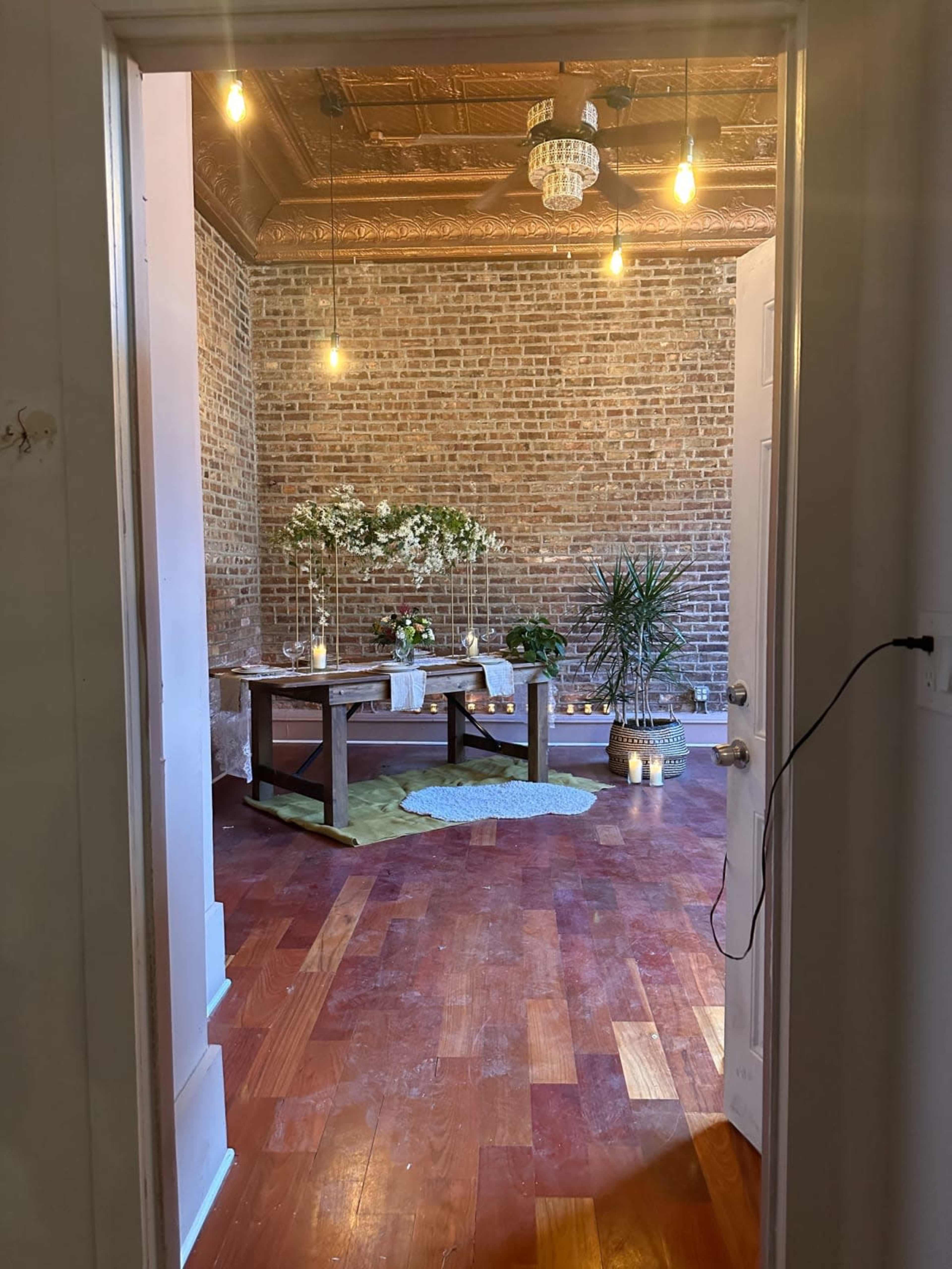 A spacious room with exposed brick walls, wooden flooring, and a wooden table surrounded by plants and decorative elements.