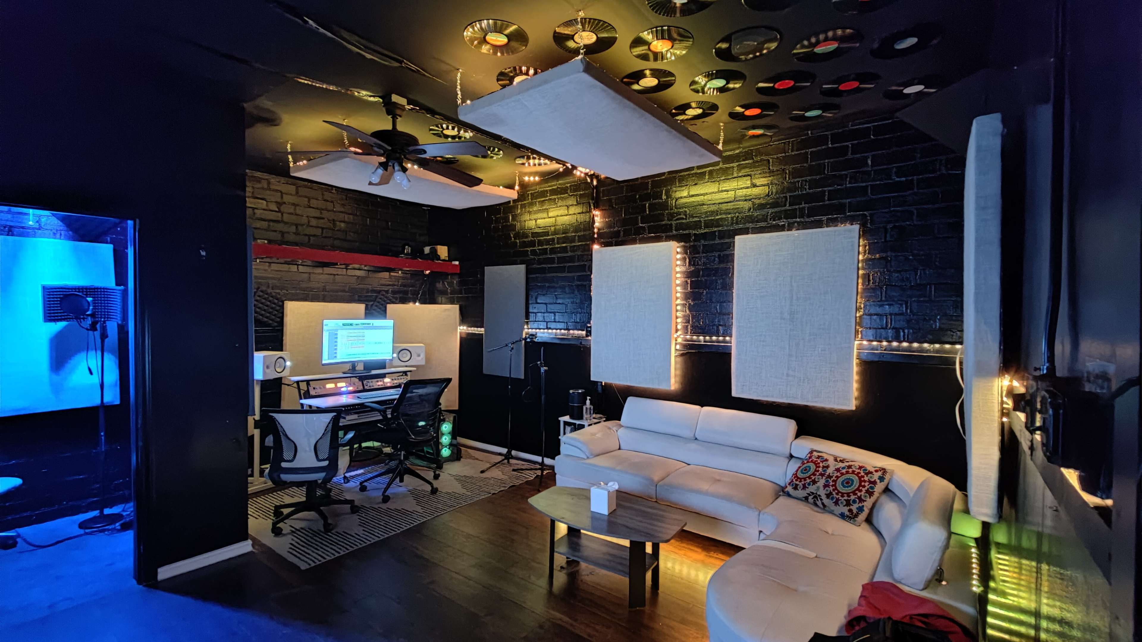 A modern recording studio featuring a comfortable seating area, soundproofing panels, and musical equipment illuminated by ambient lighting.