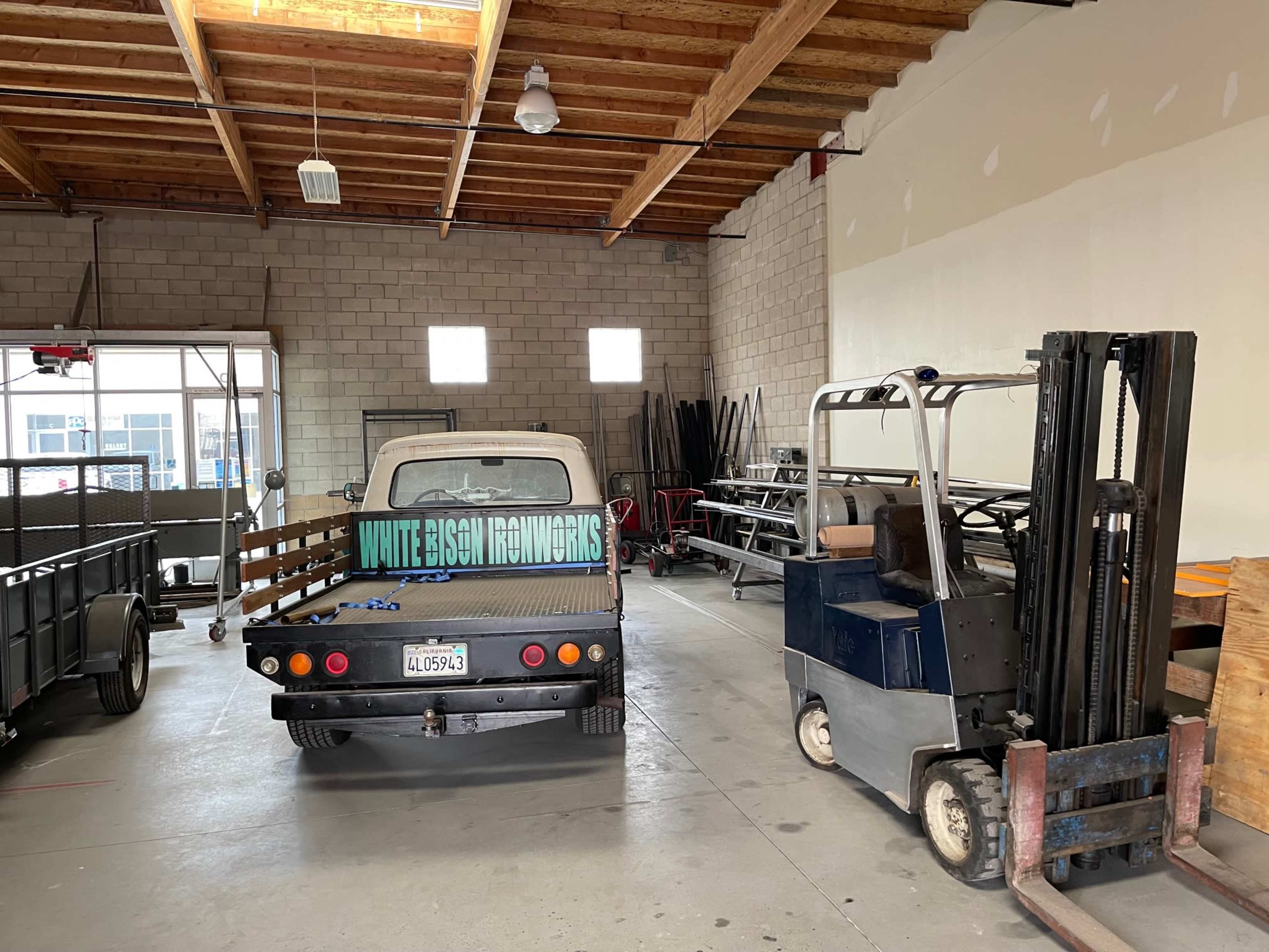 A spacious garage with a vintage truck displaying a sign reading "White Bison Renovations" parked beside a forklift.