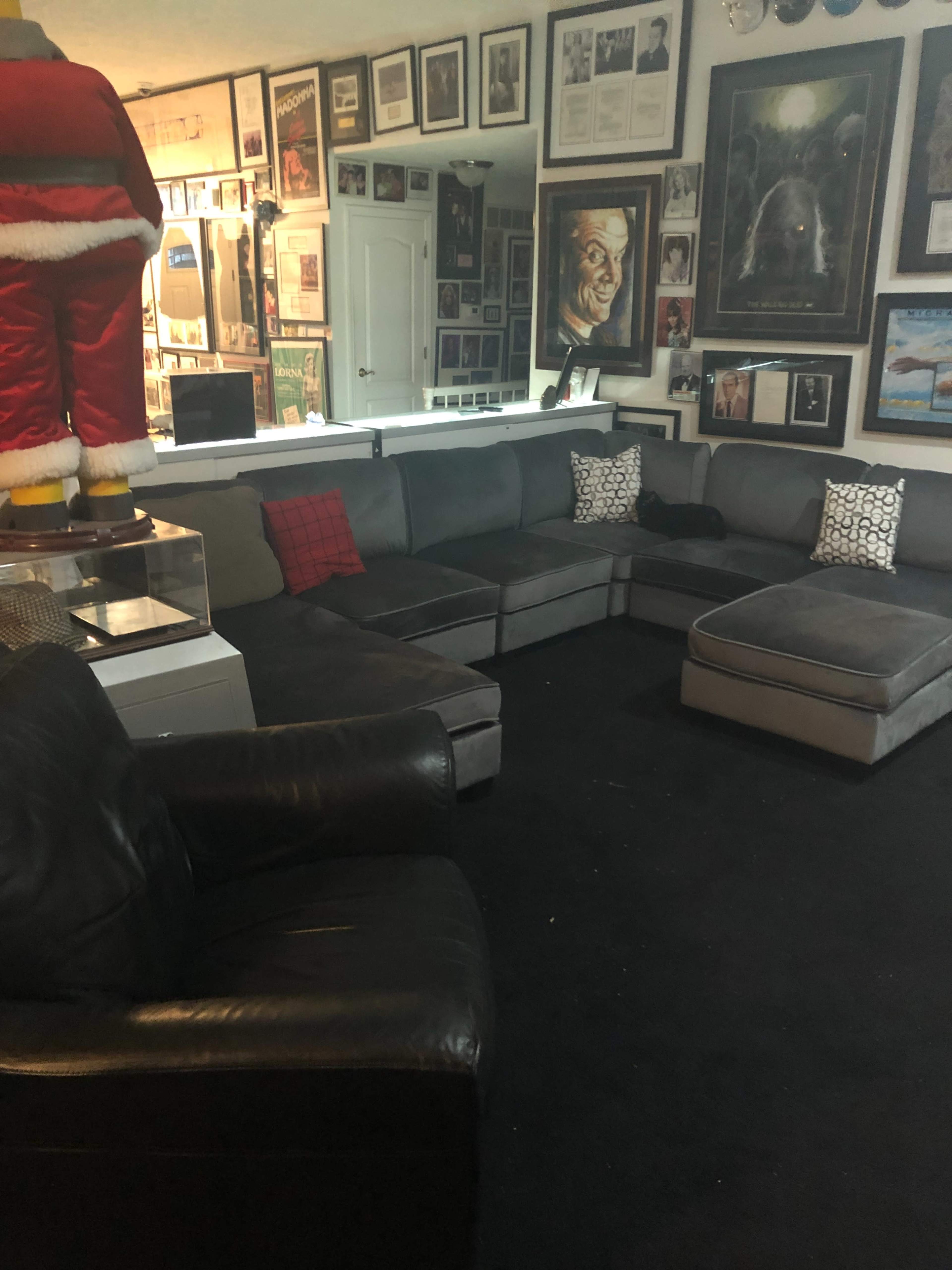 The image shows a cozy living room with a large sectional sofa, a black armchair, and numerous framed pictures and artwork adorning the walls.