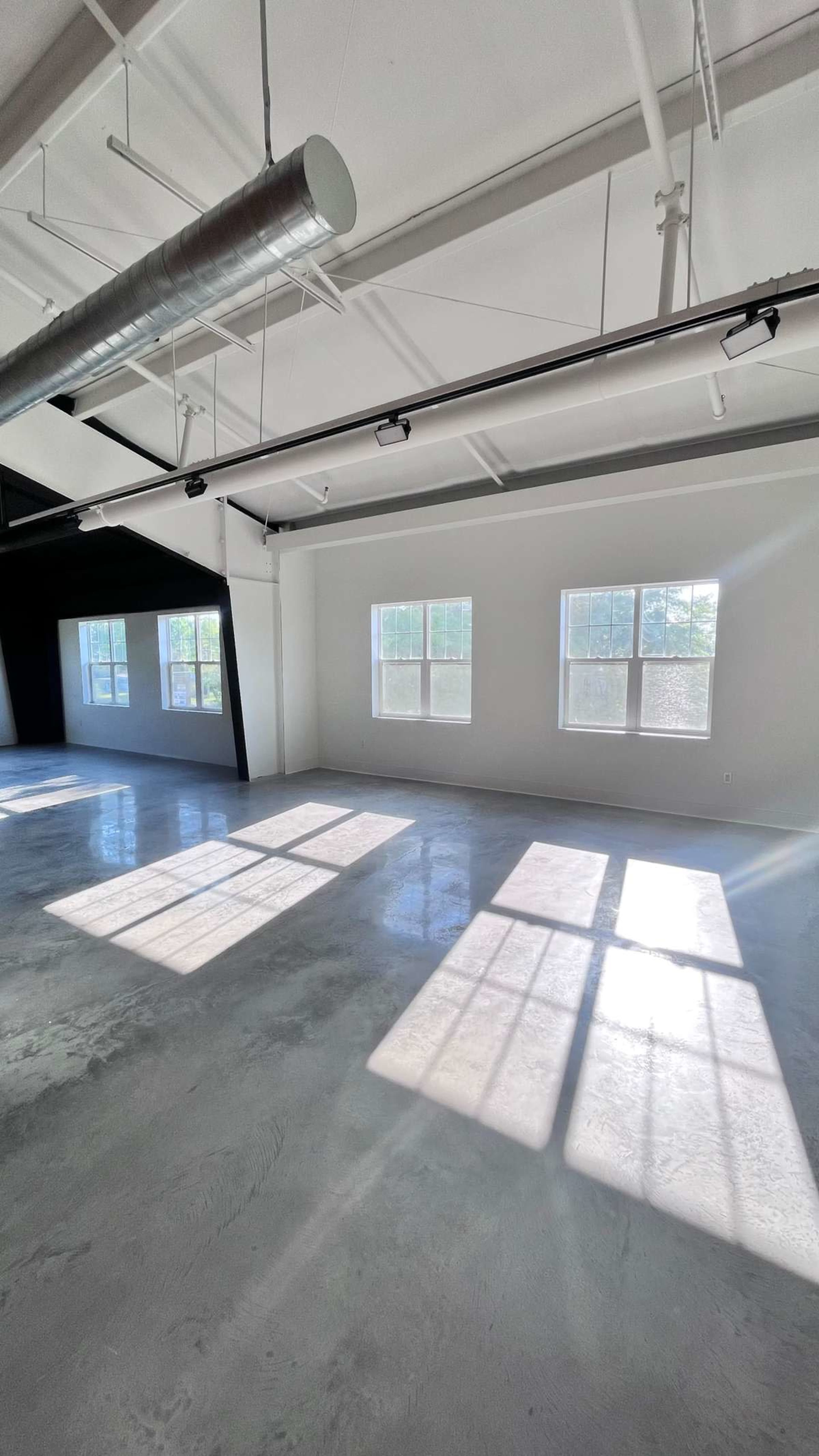 The image shows a spacious, empty room with two large windows casting shadows on a polished concrete floor.