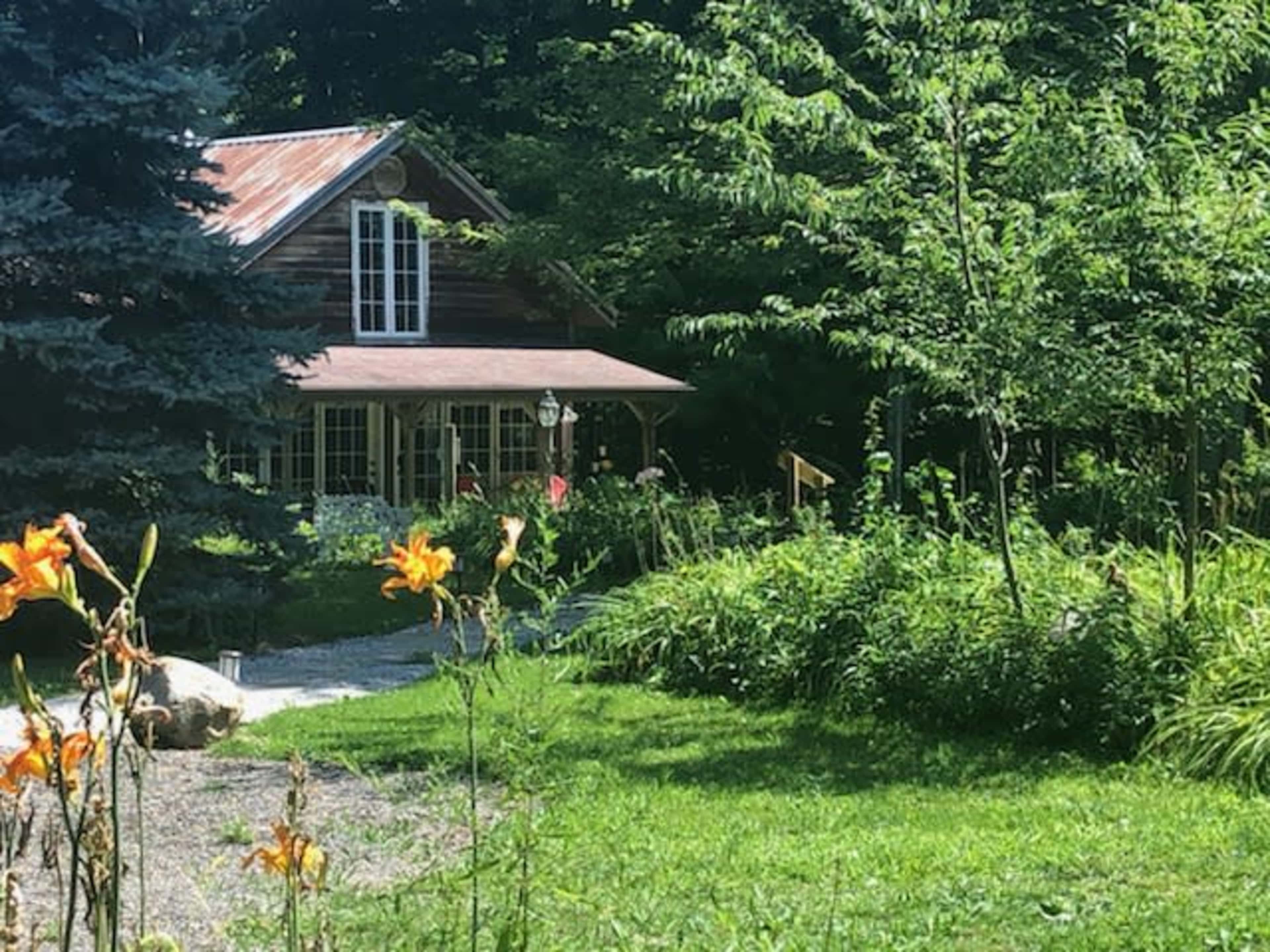 A wooden cabin with a metal roof is surrounded by lush greenery and colorful flowers.