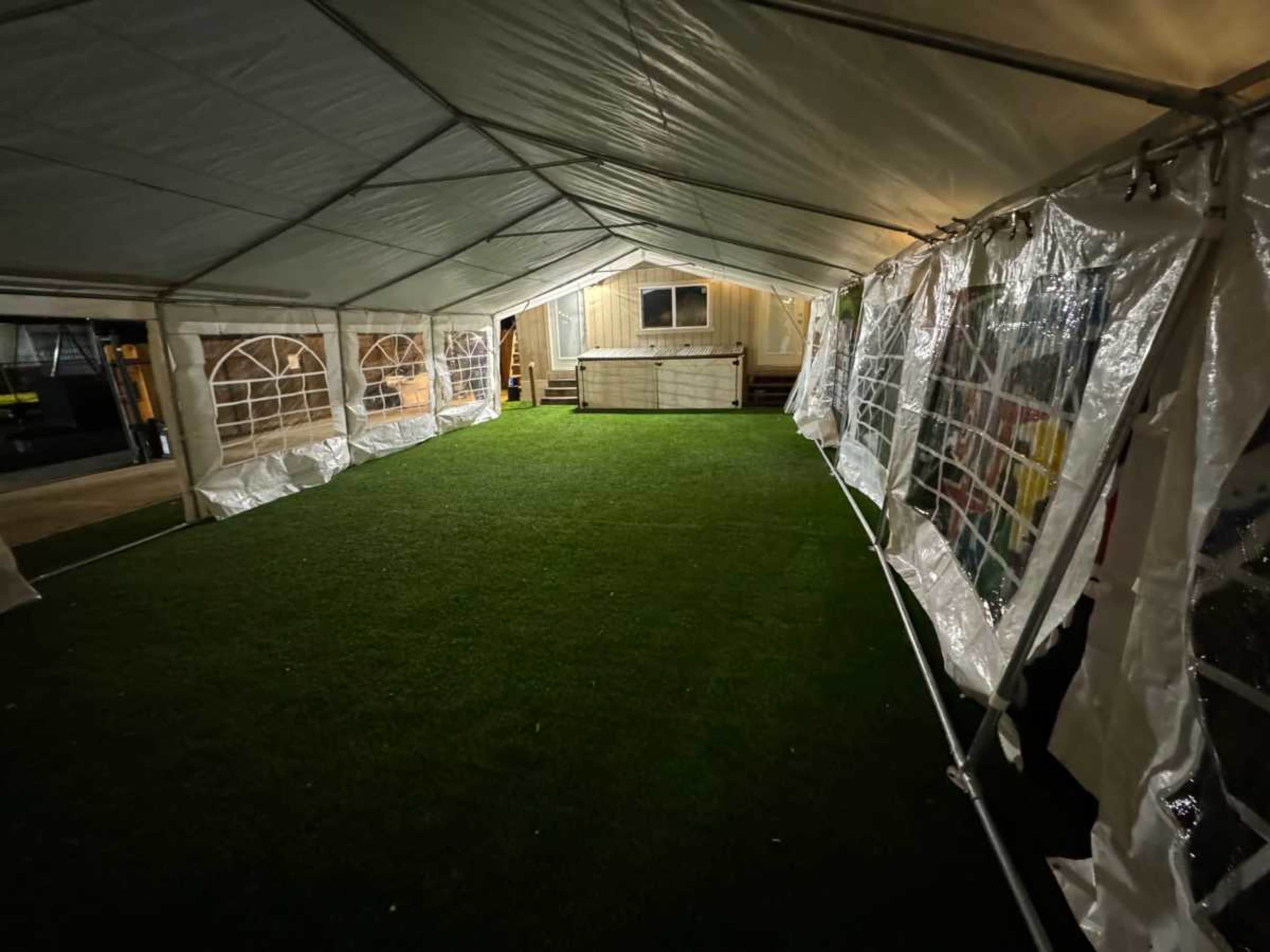 A large, empty tent with a grass-like floor and open sides is set up to provide shelter in an outdoor space.