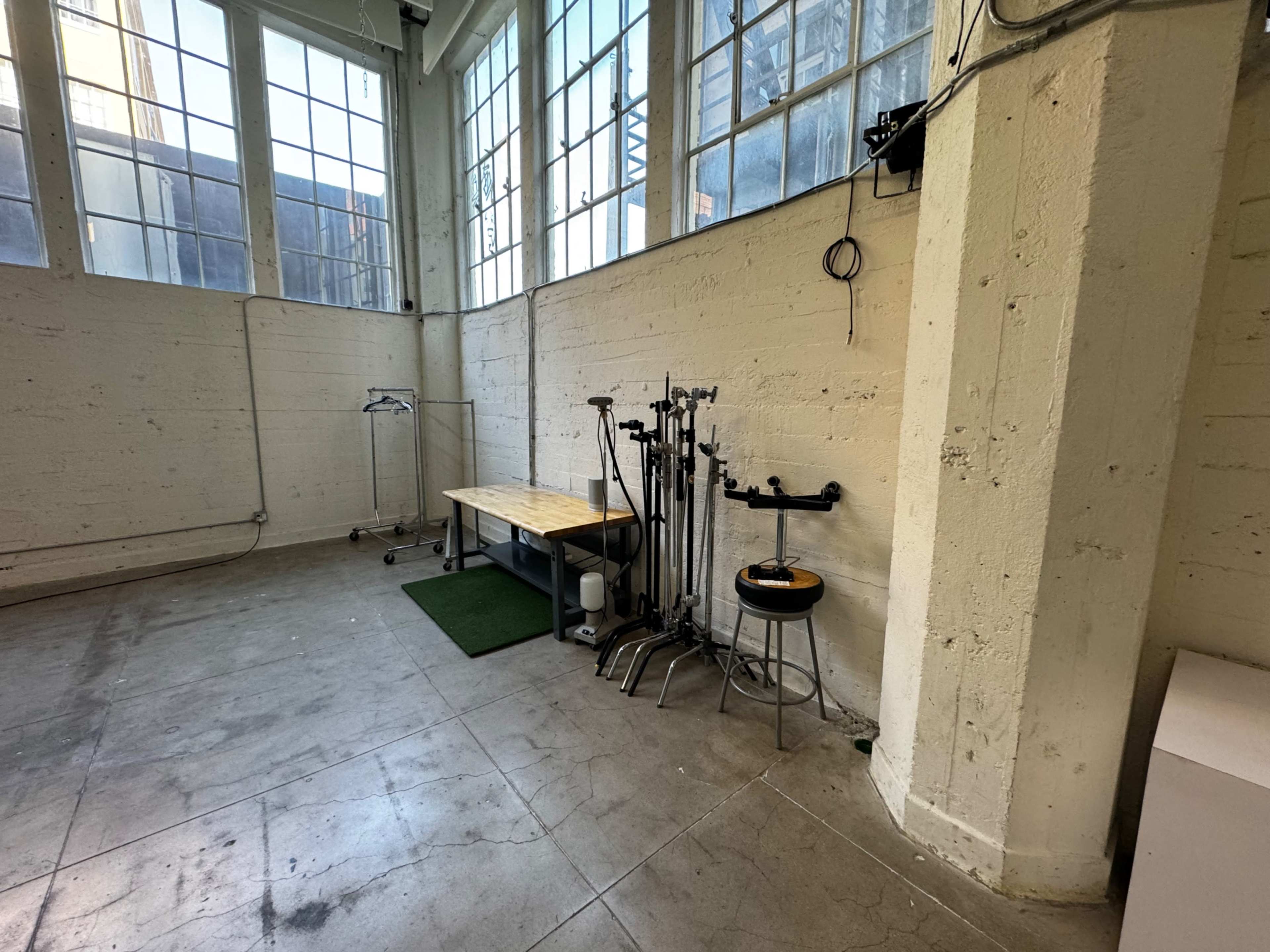 A sparse, industrial-style room with large windows, a wooden table, and various equipment on stands along the walls.