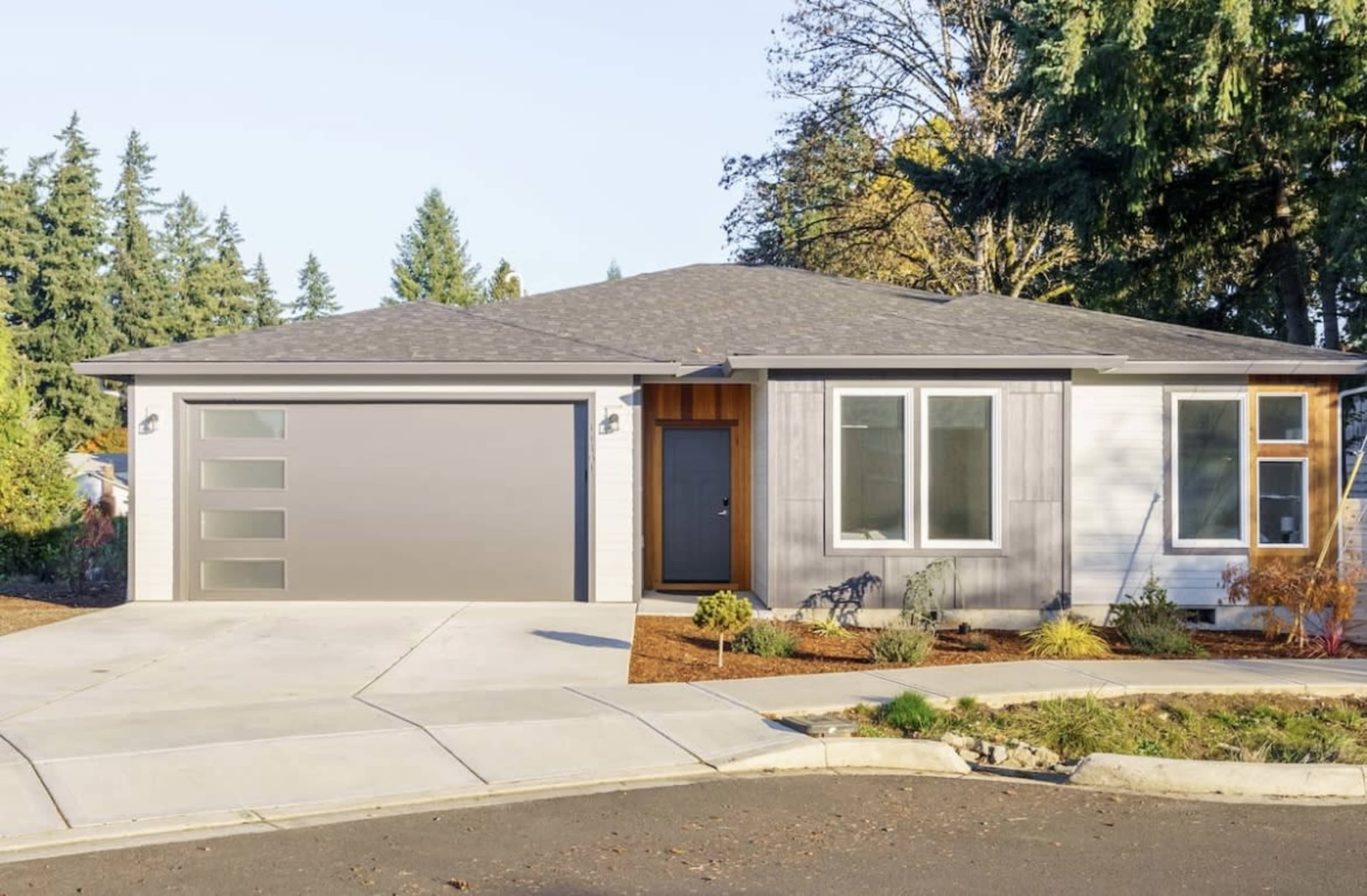 A modern single-story house with a gray exterior, a large garage door, and a neatly landscaped front yard.