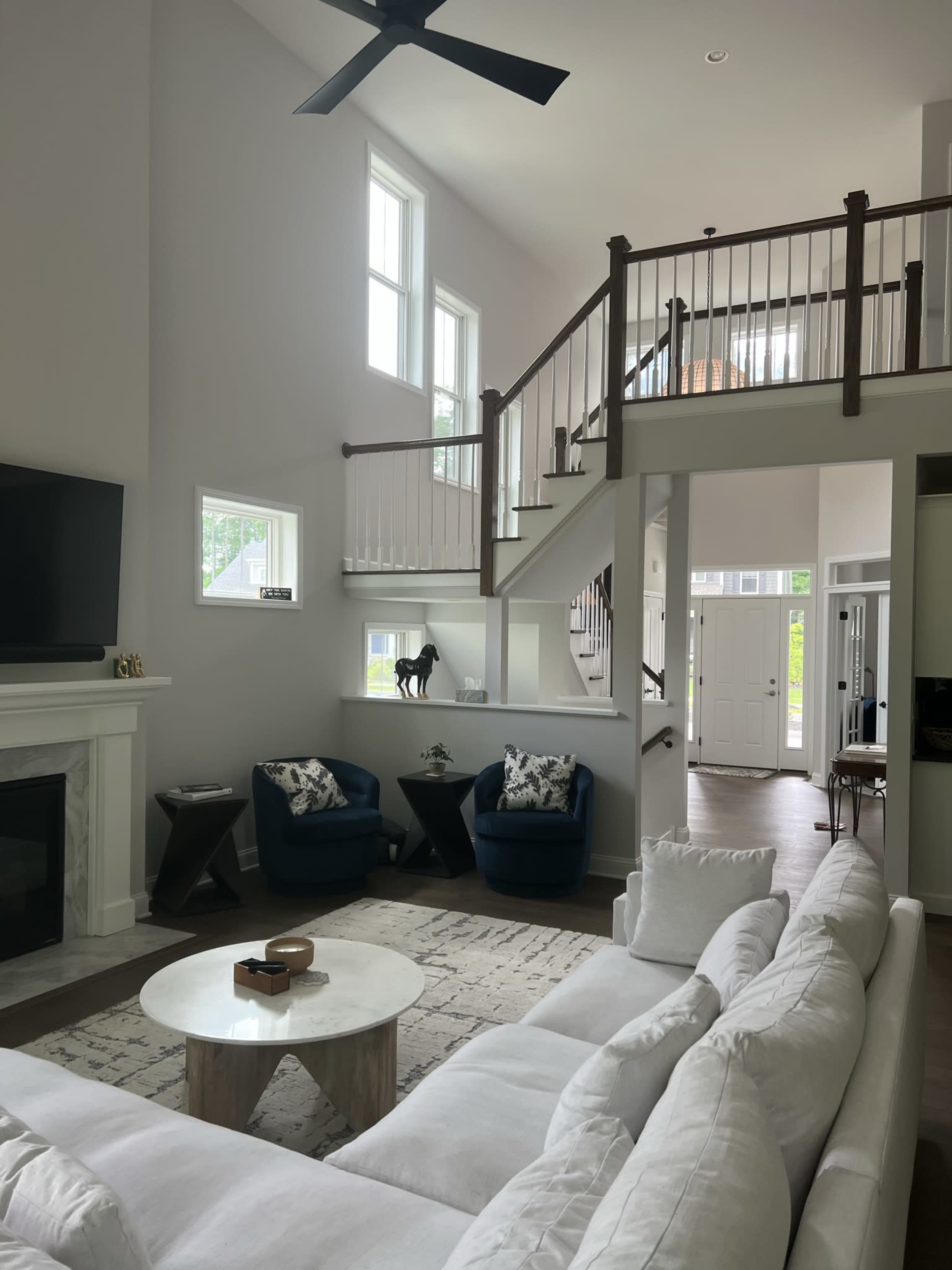 A modern living room with a white sofa, two blue chairs, a round coffee table, and a staircase leading to an upper level.