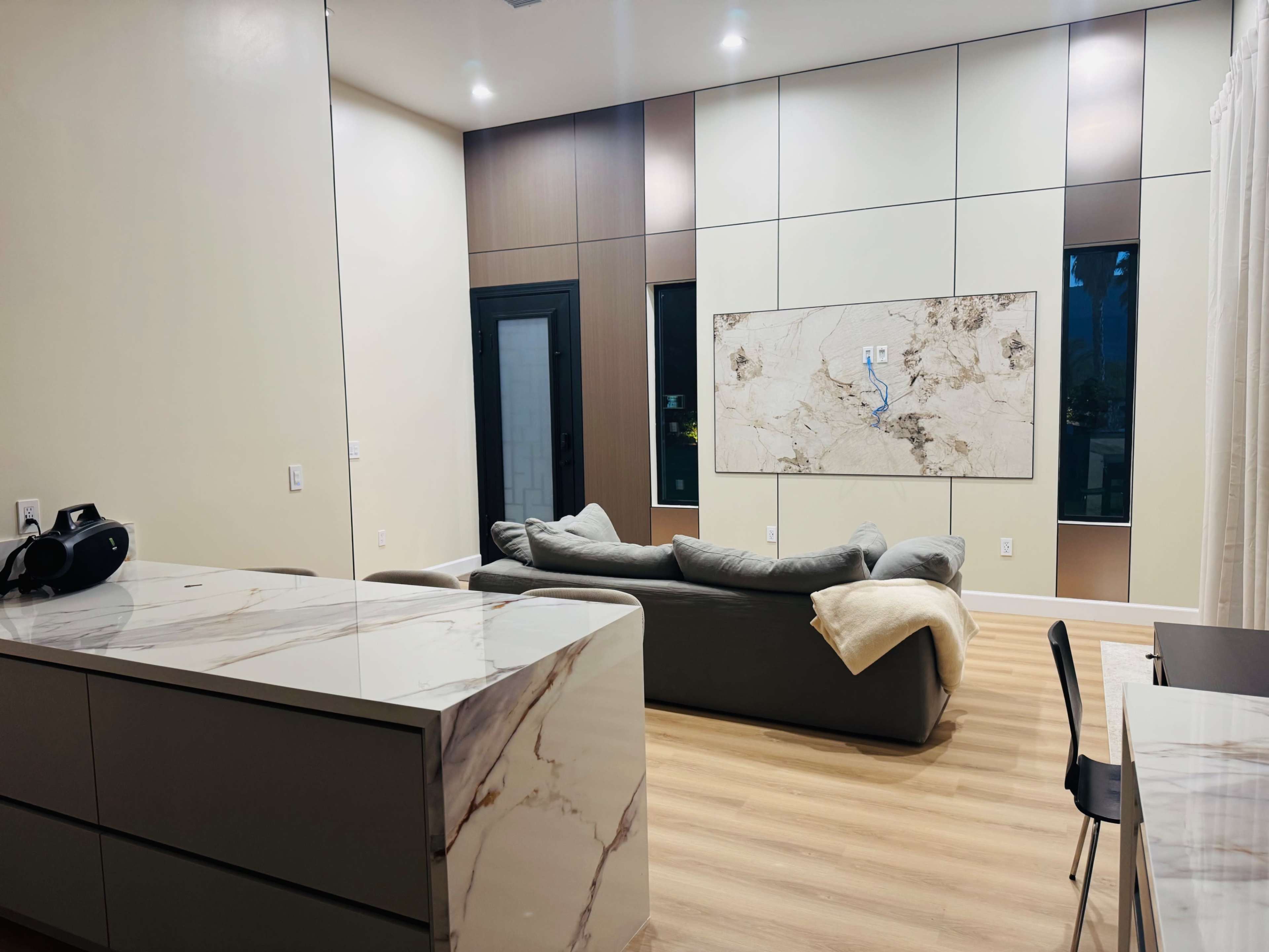 The image shows a modern living room with a gray sofa, a marble kitchen island, and a large wall-mounted artwork.