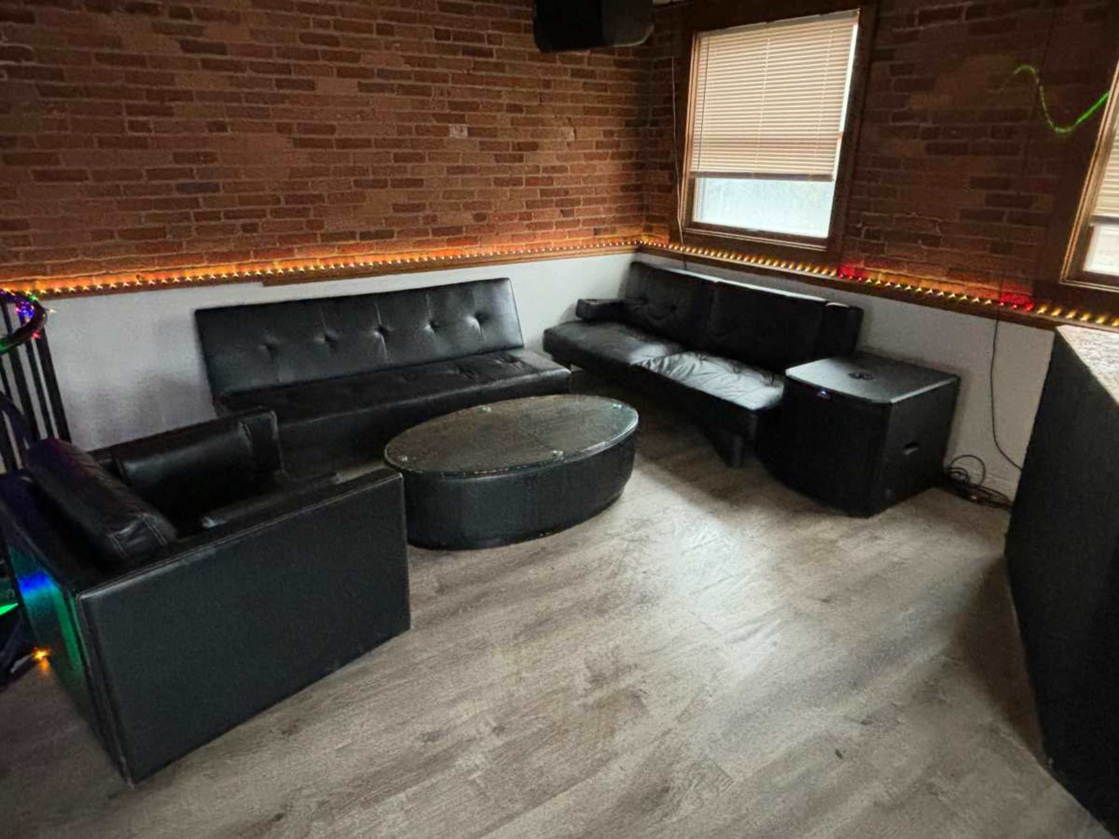 A lounge area features black sofas and a circular coffee table, with brick walls and wooden flooring.