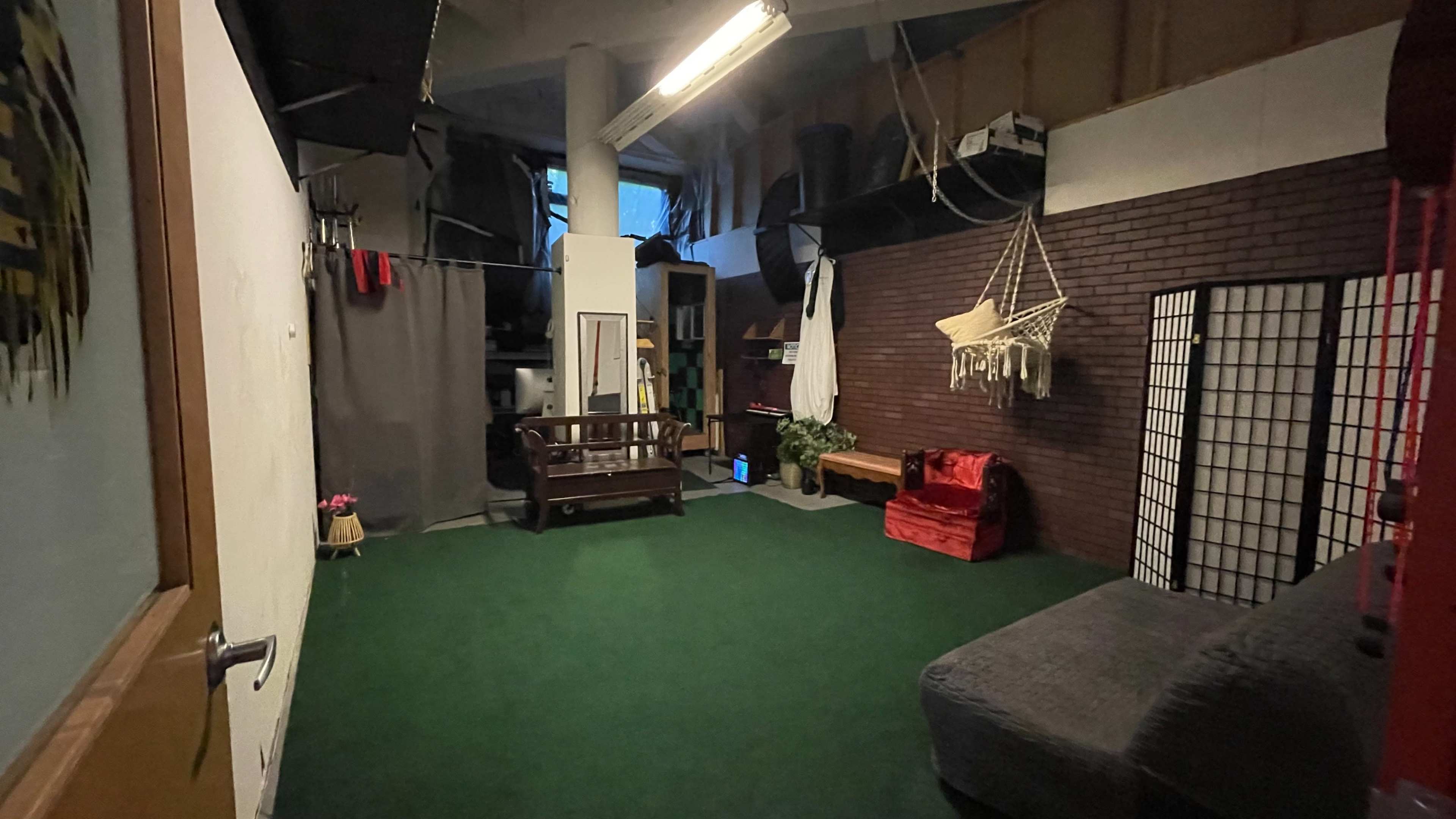 The scene shows a room with green carpet, a wooden bench, a red chair, a hanging chair, and partitions against a brick wall.