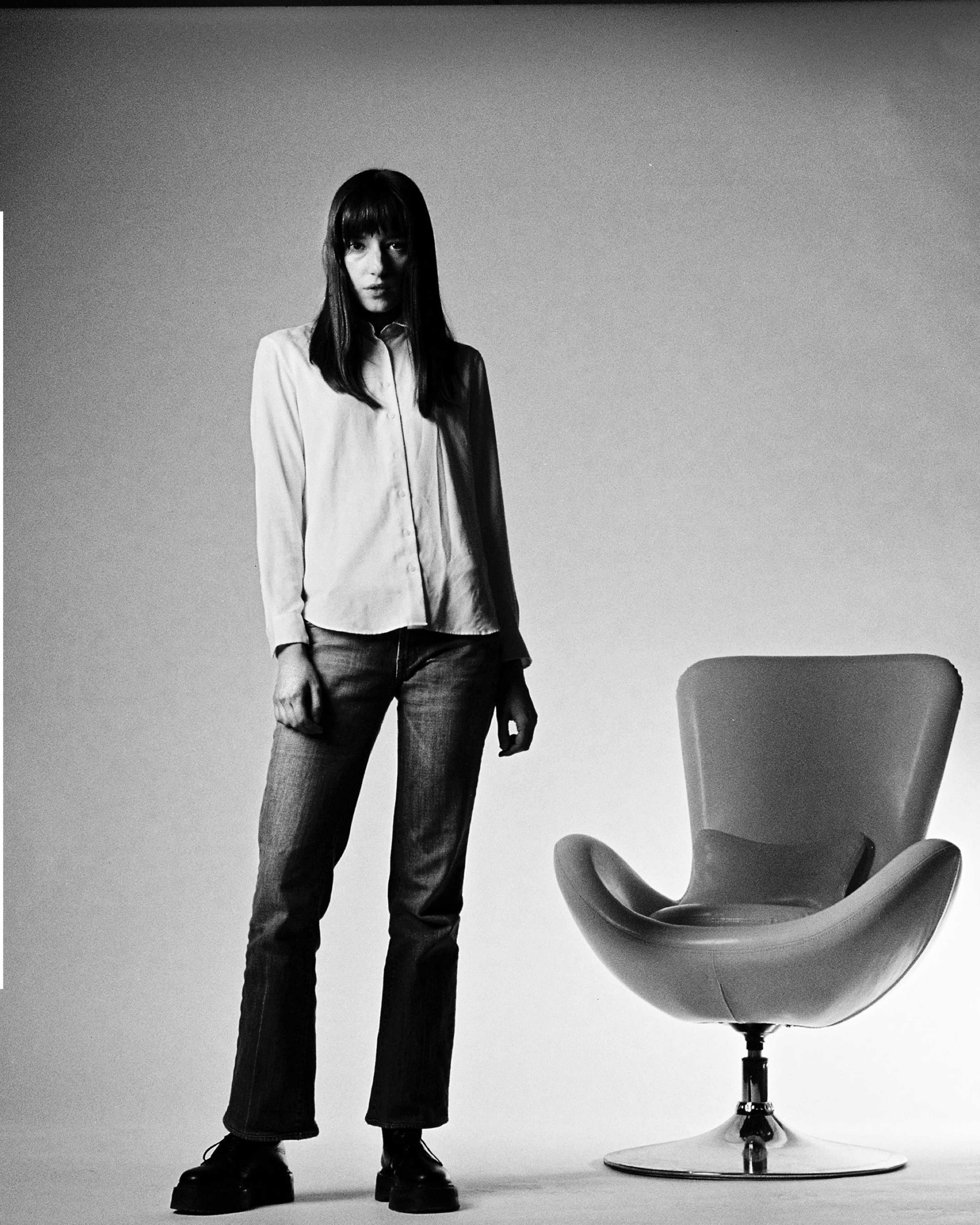 A person stands next to a modern chair against a plain background.