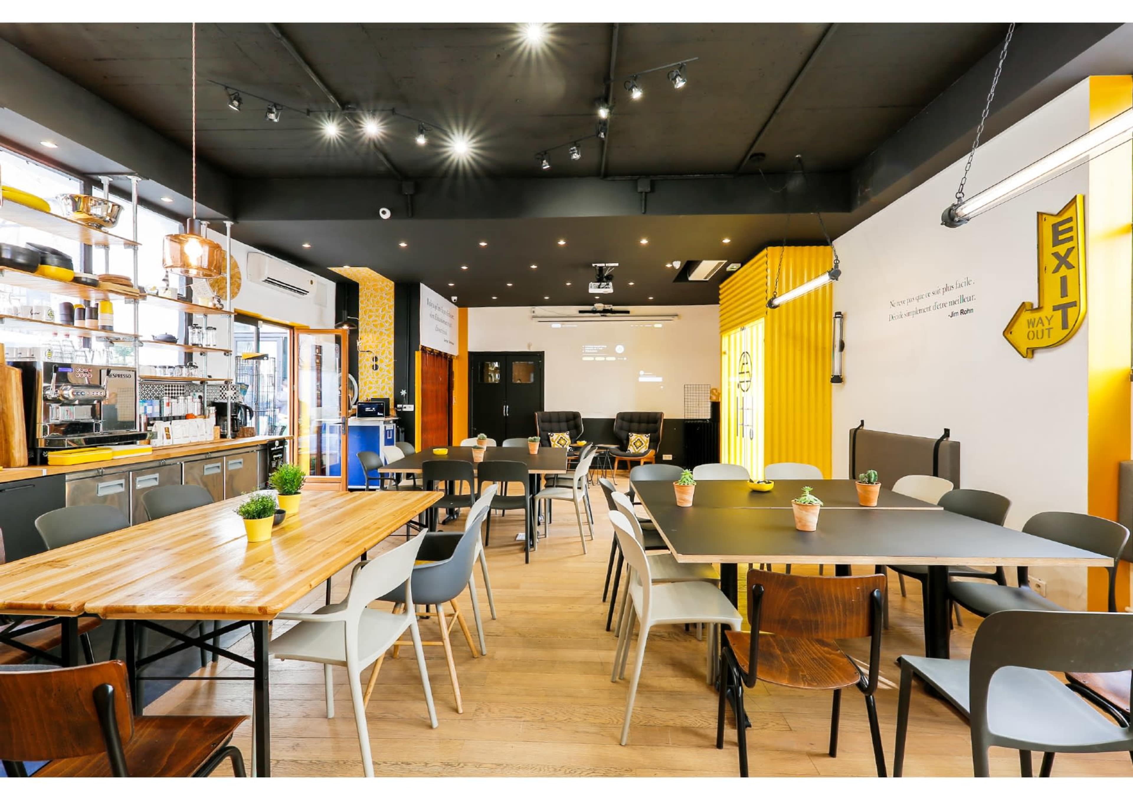 A modern cafe interior with wooden and metal tables, minimalist decor, and a coffee counter in the background.